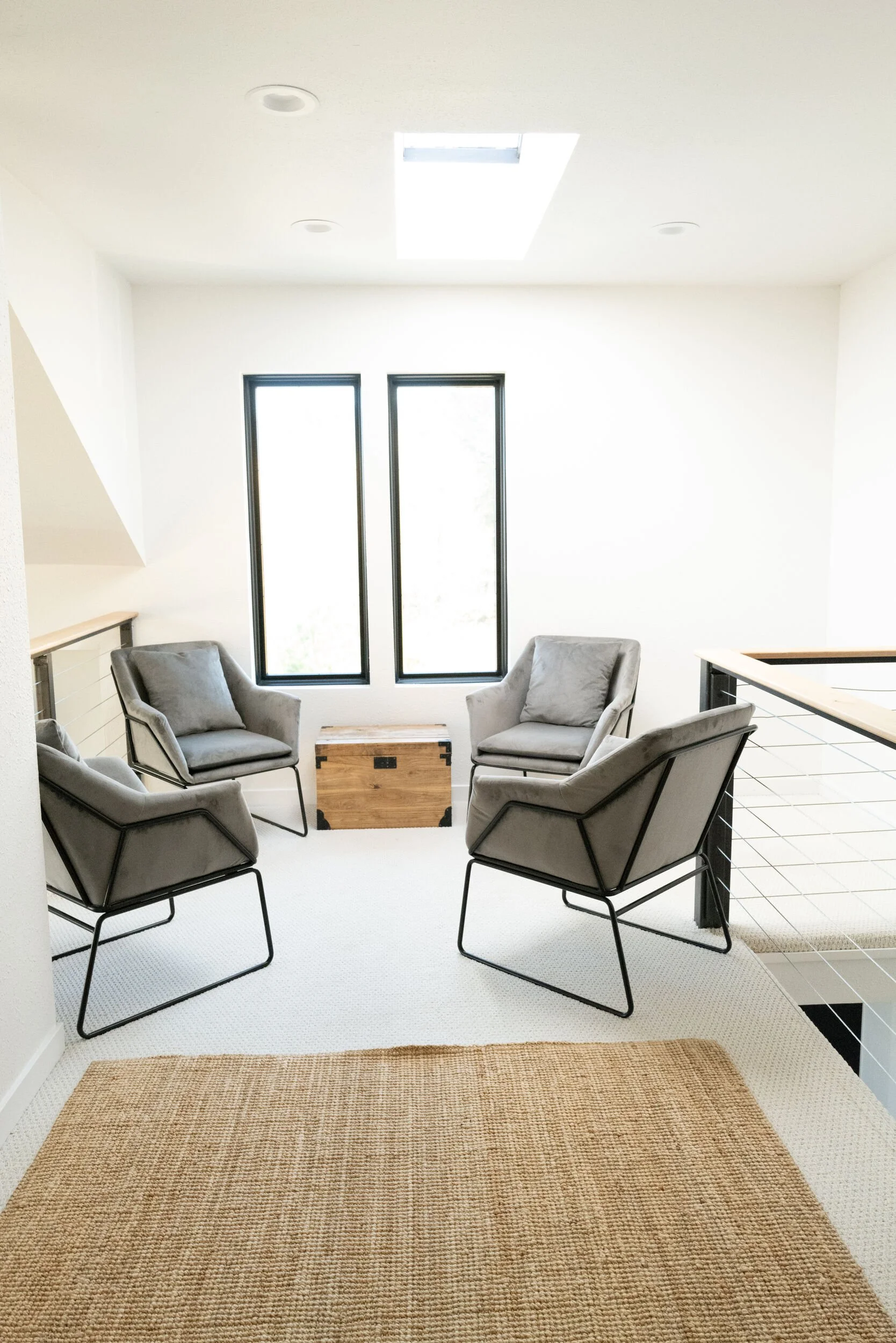 Bright white living room with gray lounge chairs and a jute rug under a skylight in Hot Sulphur Springs, Colorado