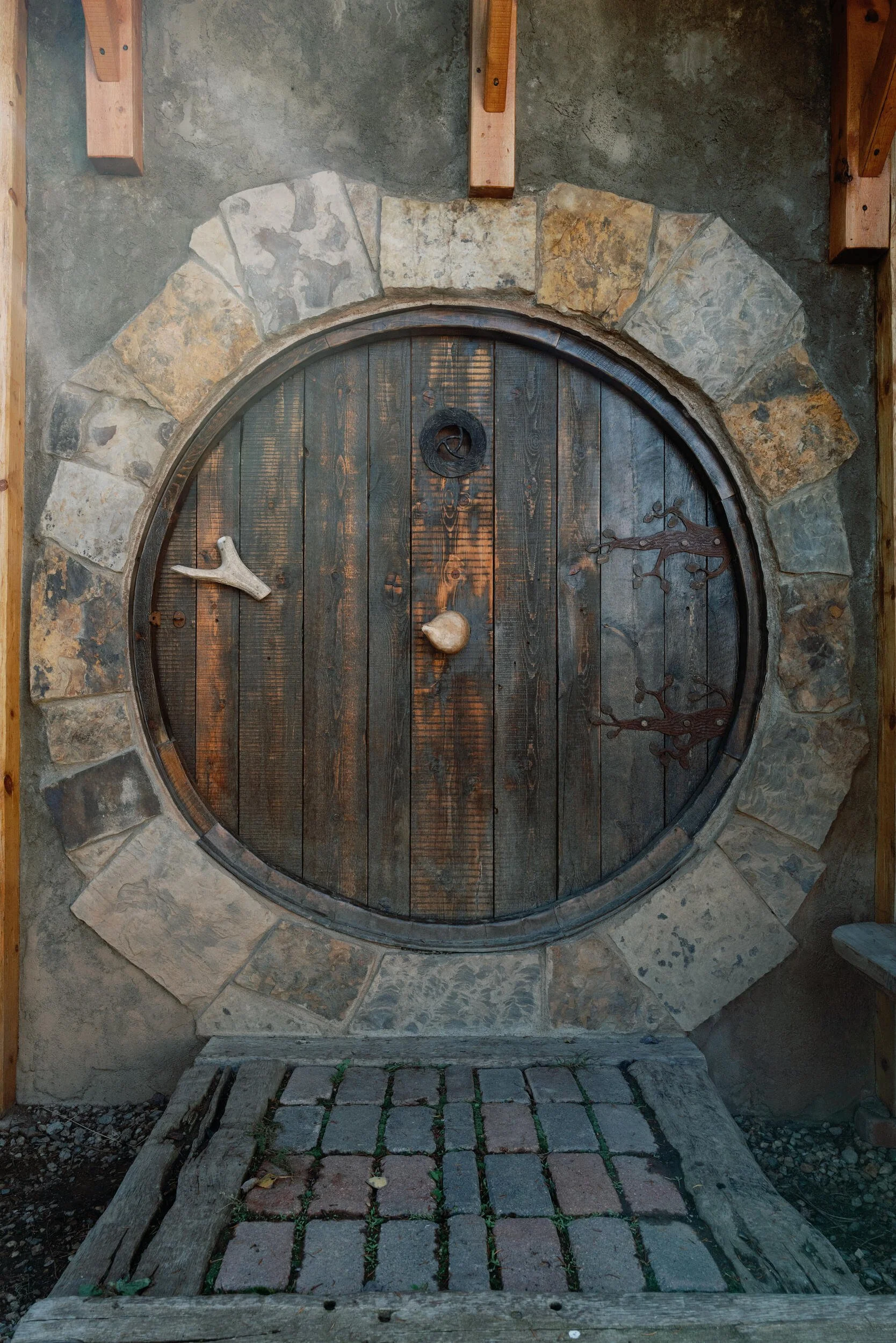 Round wooden door in a stone archway at the Hobbit Hole, reached by a plank walkway, in Hot Sulphur Springs, Colorado