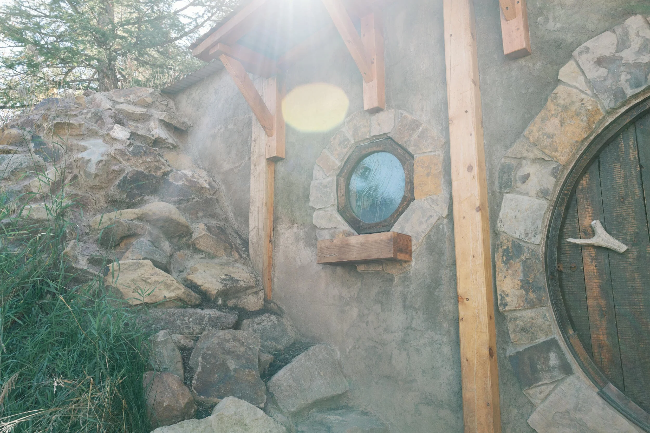 Stone-walled Hobbit Hole entry with a round wooden door and small round window in Hot Sulphur Springs, Colorado