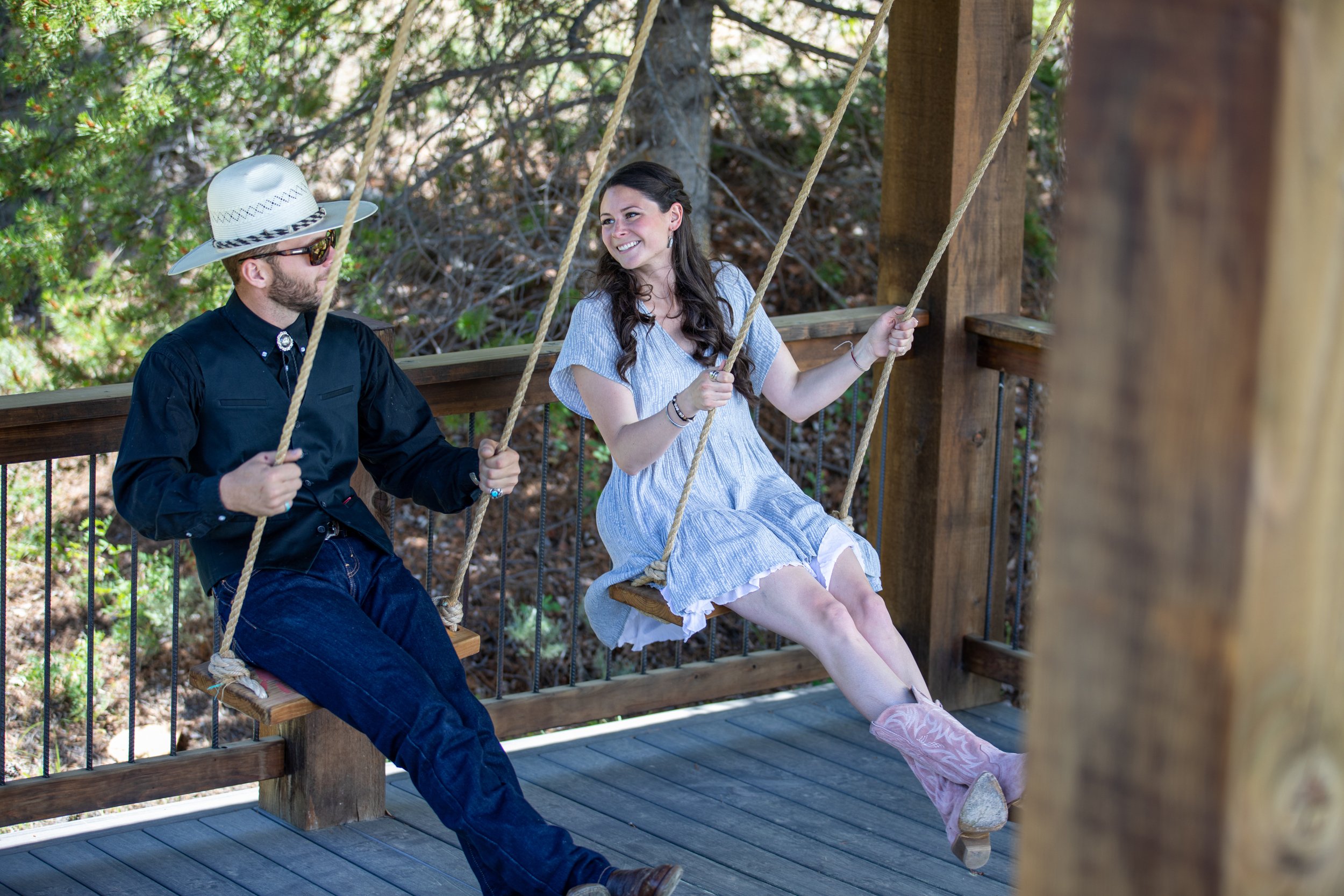 Man in a cowboy hat and woman in a white dress on a wooden swing at Tundra Springs, Colorado mountain wedding venue