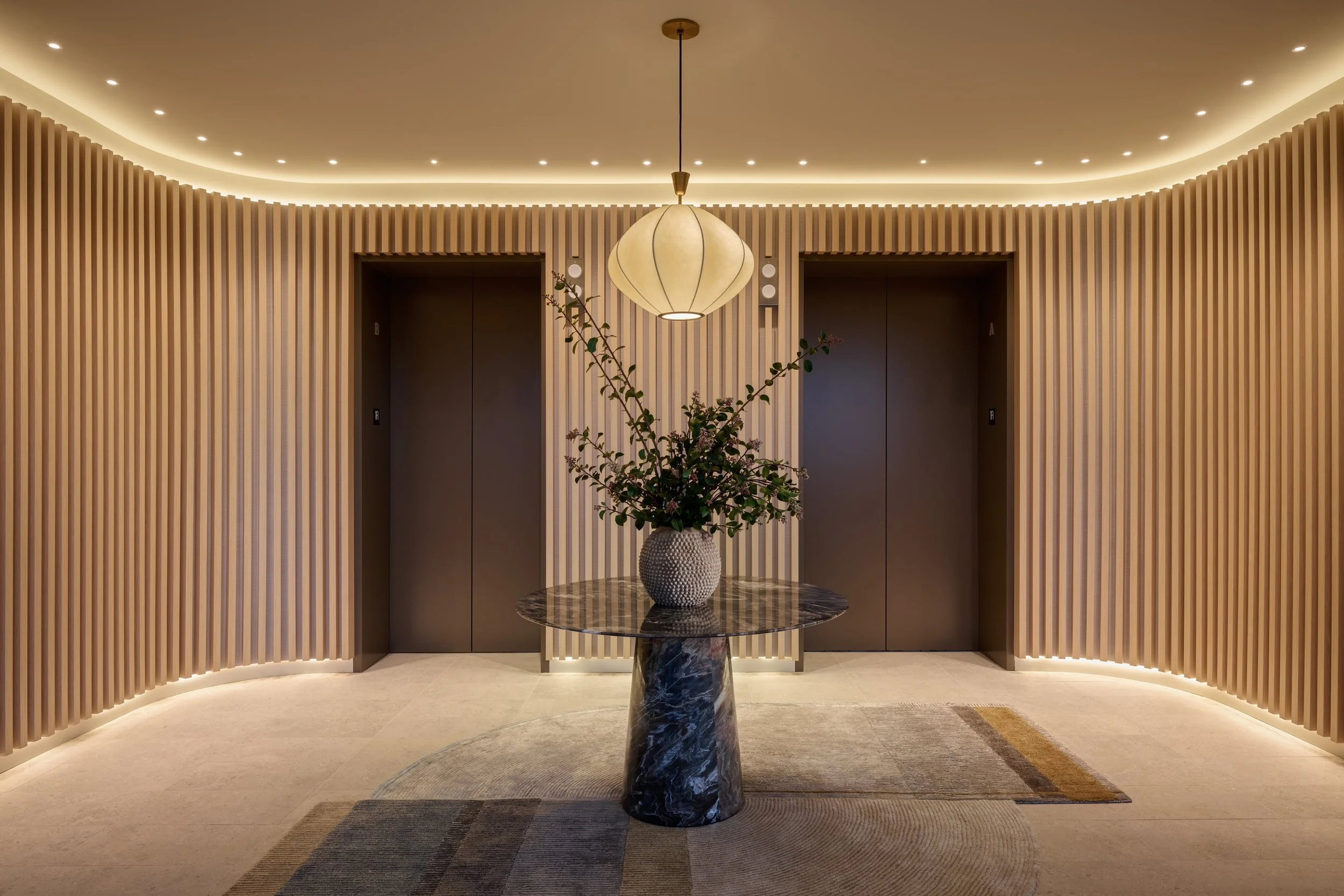 Elevator lobby wrapped in wood slats with a cove-lit ceiling and a pendant over a floral table, 490 Avenue of the Palms, Treasure Island