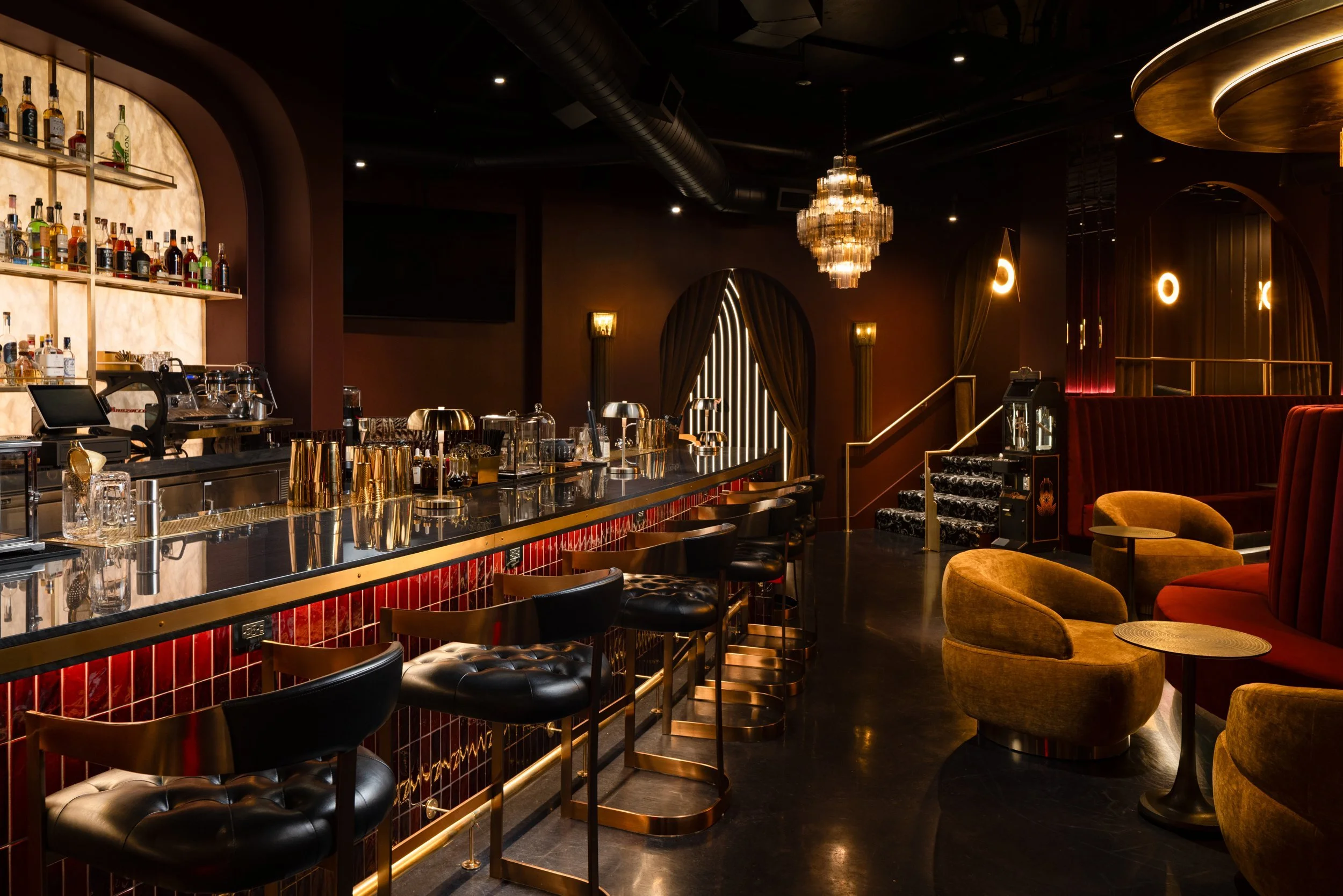 Bar with tufted leather stools and red tile, opening onto a lounge of mustard velvet chairs and a crystal chandelier, Matrix Bar, Napa