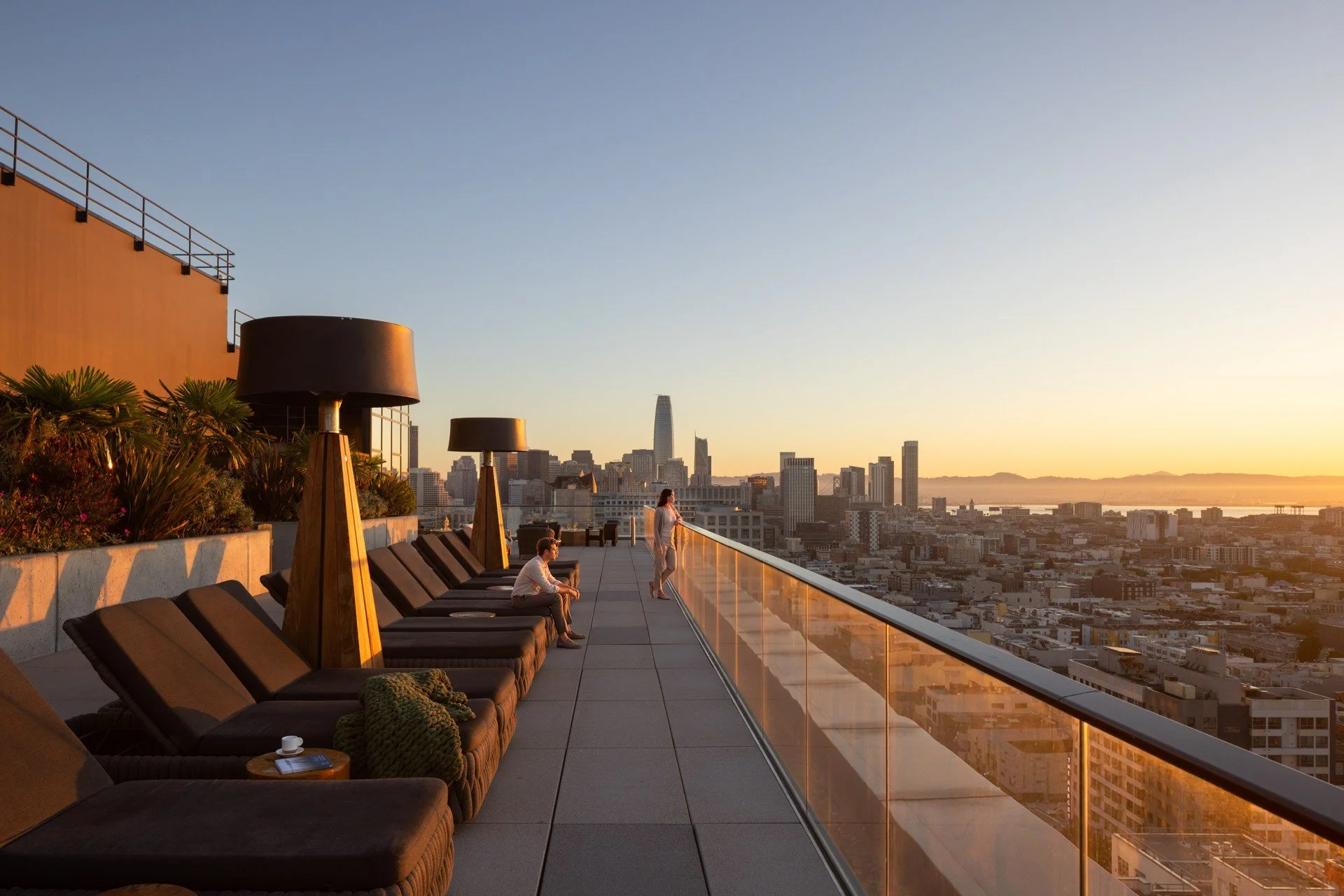 Rooftop sun deck with loungers and a glass rail at sunset looking toward downtown San Francisco, NEMA