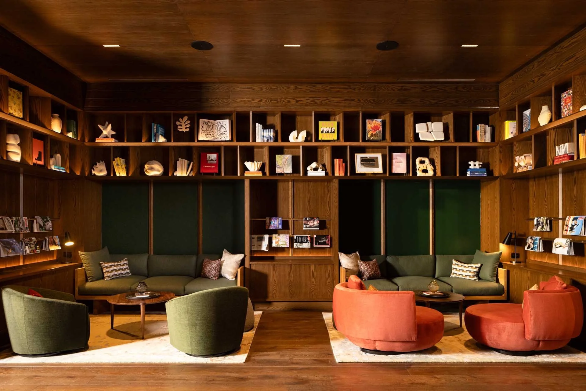 Wood-paneled library with floor-to-ceiling bookshelves and coral and green armchairs, The Clara, Santa Clara