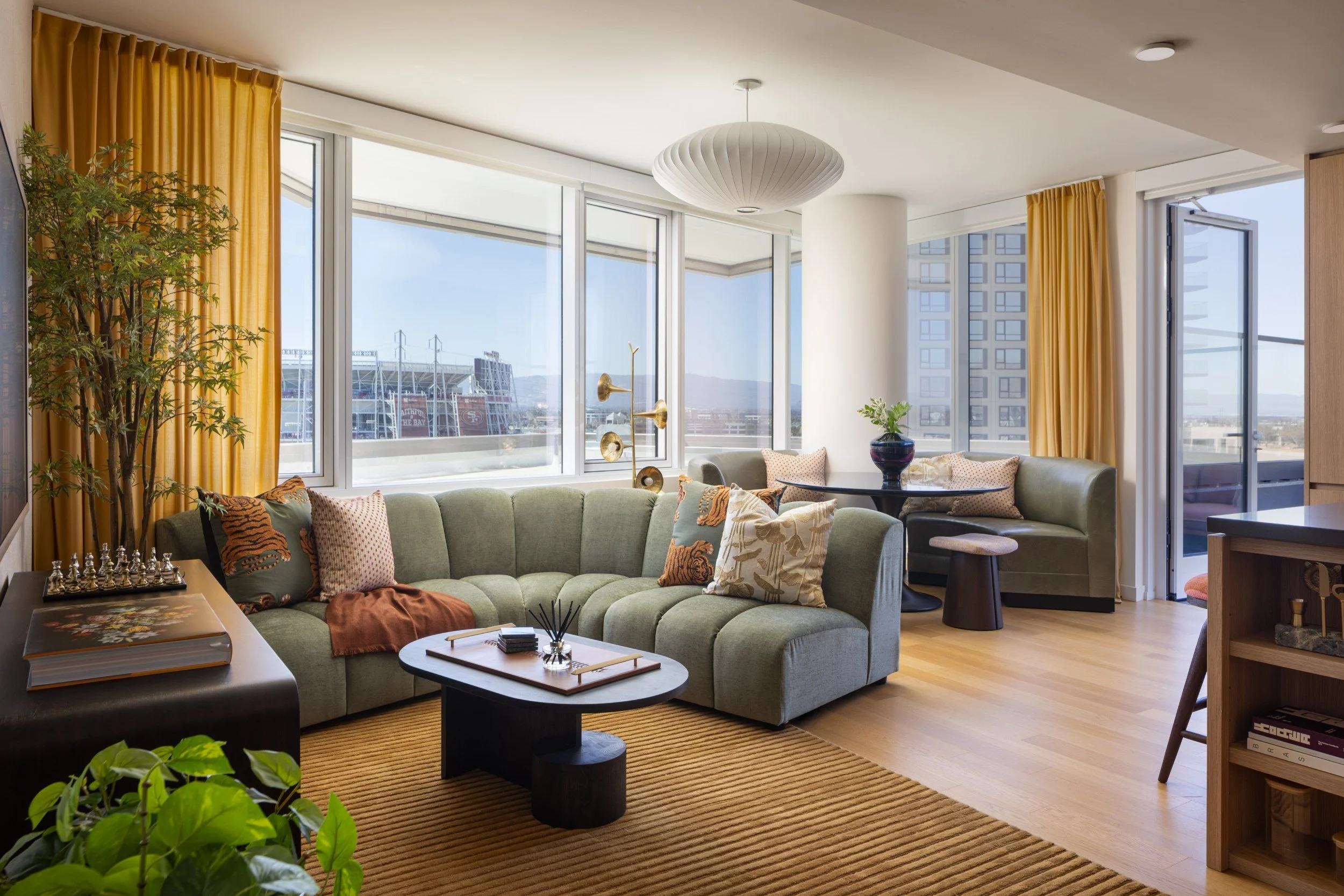 Residence living room with a sage sectional, round coffee table and corner windows, The Clara, Santa Clara