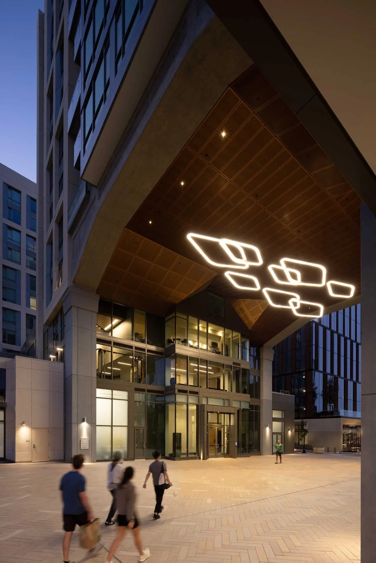 Building entry at dusk with a sculptural light fixture under the wood soffit, The Martin, Sunnyvale