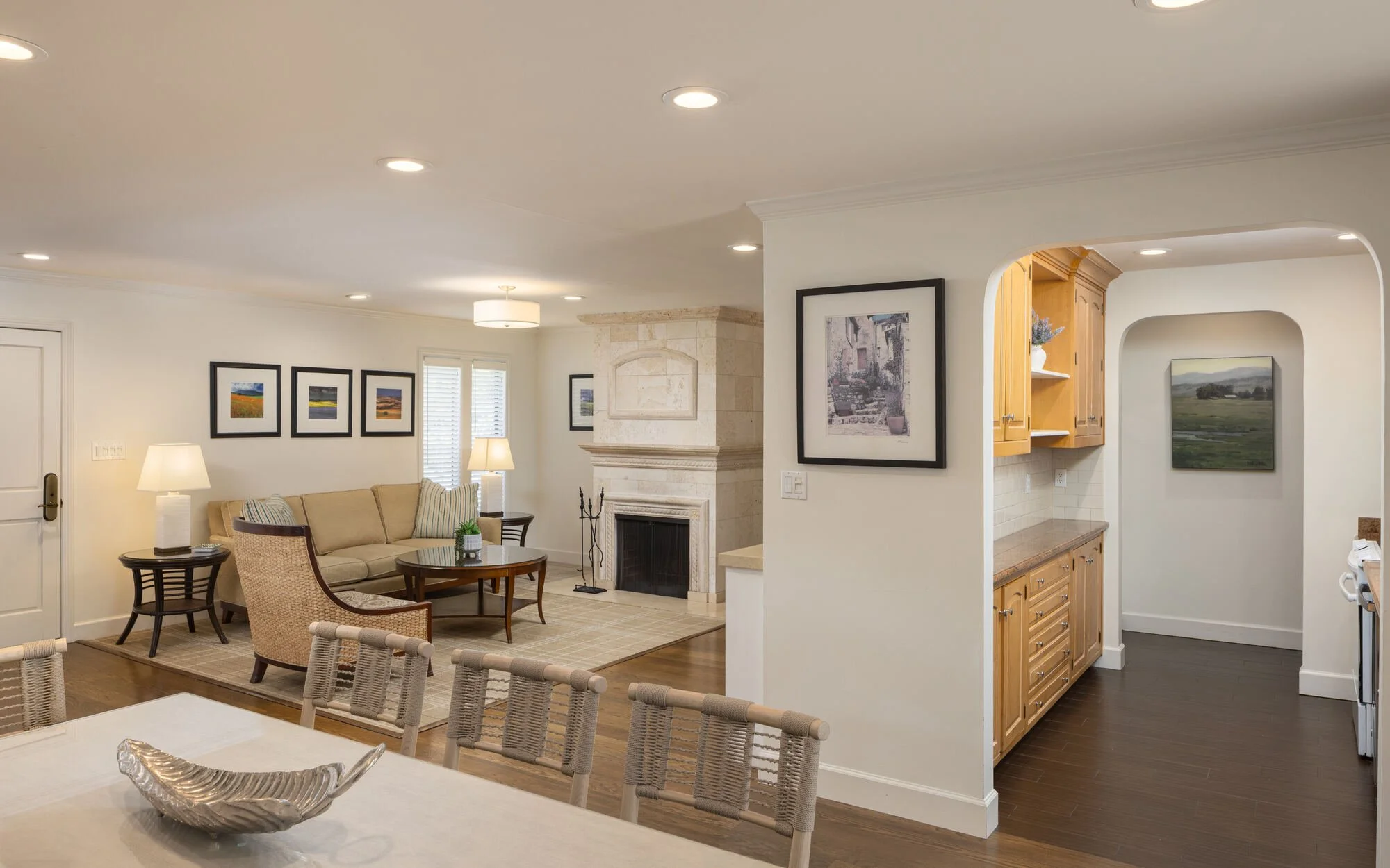 Bright open-concept home interior with a living room, stone fireplace, kitchen cabinetry, dining island, and framed artwork.