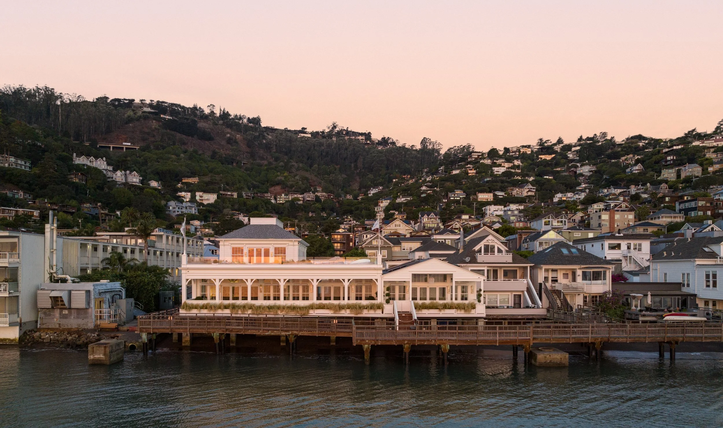 Valhalla lit at dusk on the Sausalito waterfront at 201 Bridgeway, with the hillside homes above Richardson Bay