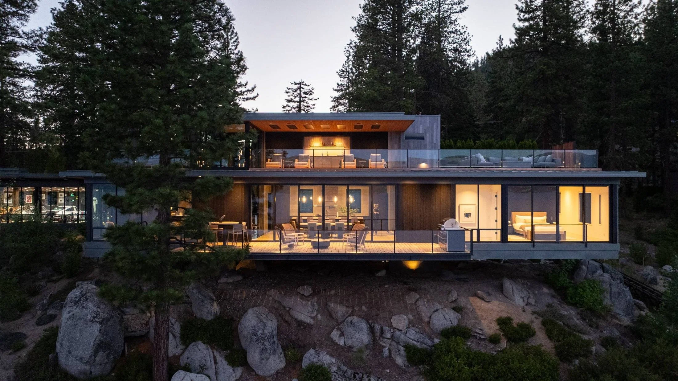 Main house glowing at dusk, set into granite and pines, Lake Tahoe Residence