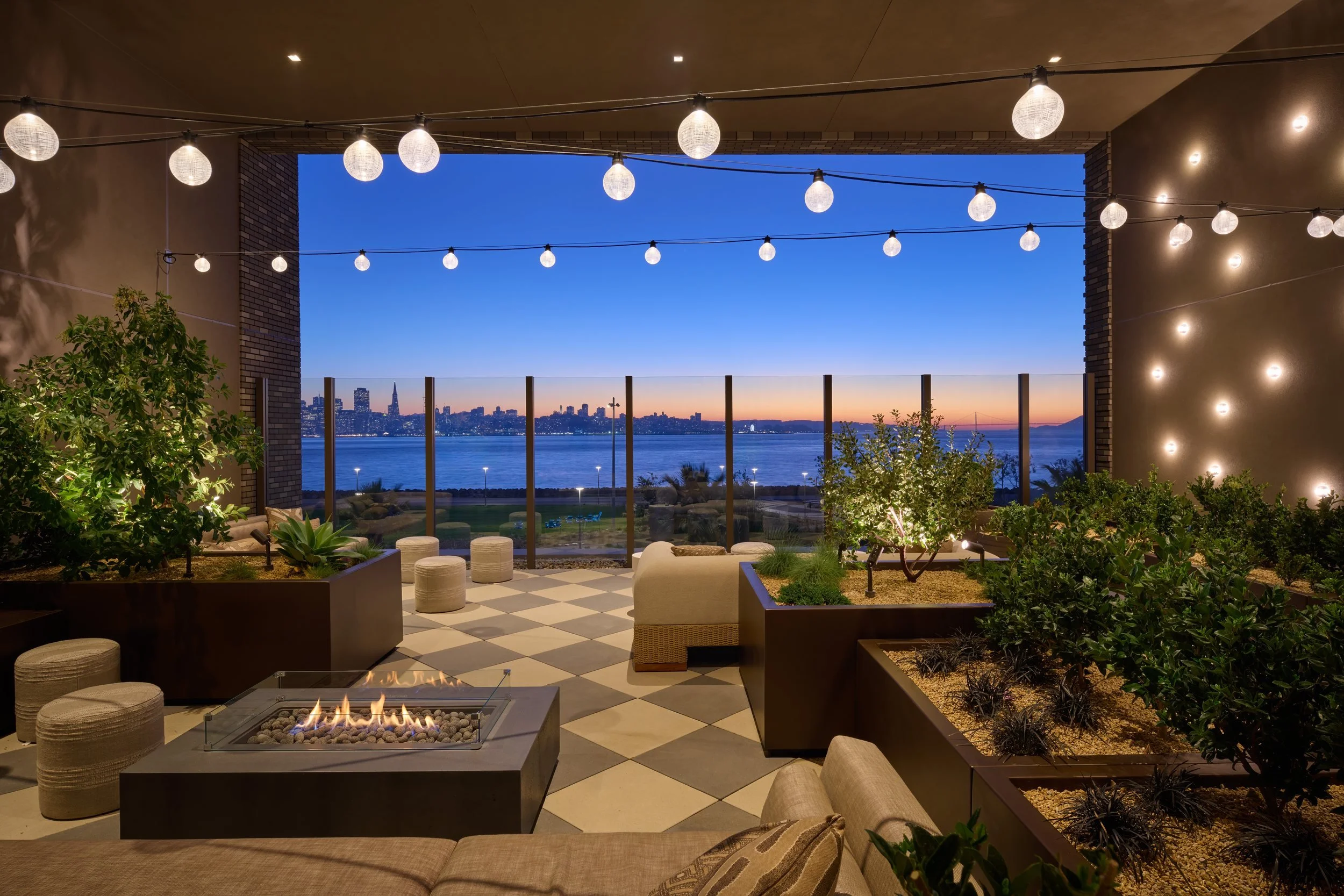 Covered roof deck with a fire table and string lights framing the skyline at blue hour, 490 Avenue of the Palms, Treasure Island