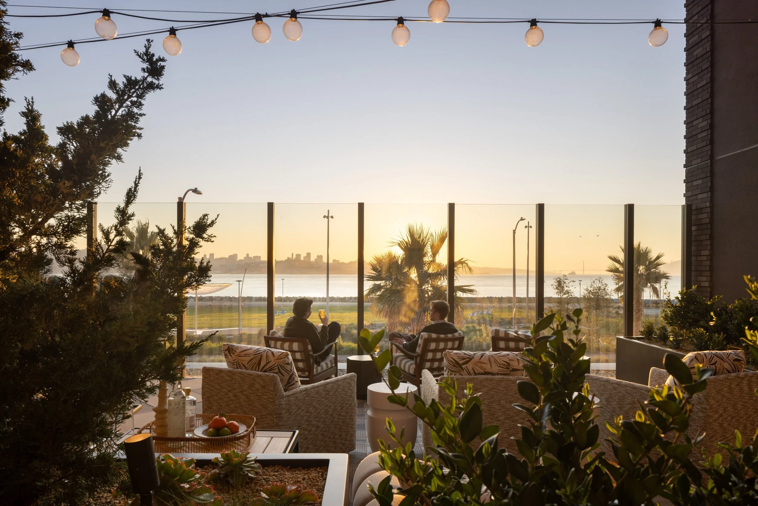 Rooftop terrace at sunset with string lights, planters and lounge seating facing the bay, 490 Avenue of the Palms, Treasure Island