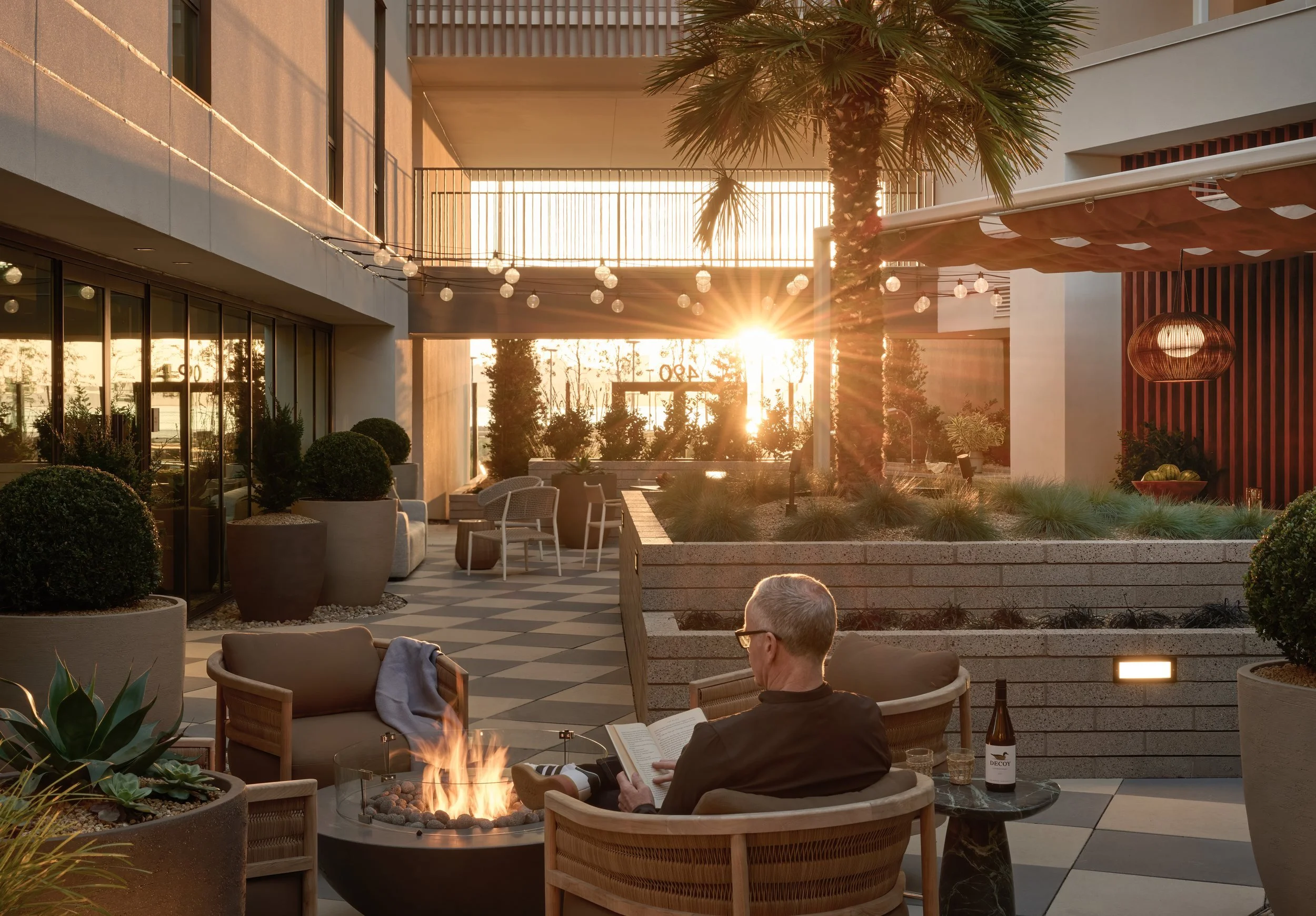 Courtyard fire pit and checkerboard pavers at golden hour with residents relaxing, 490 Avenue of the Palms, Treasure Island