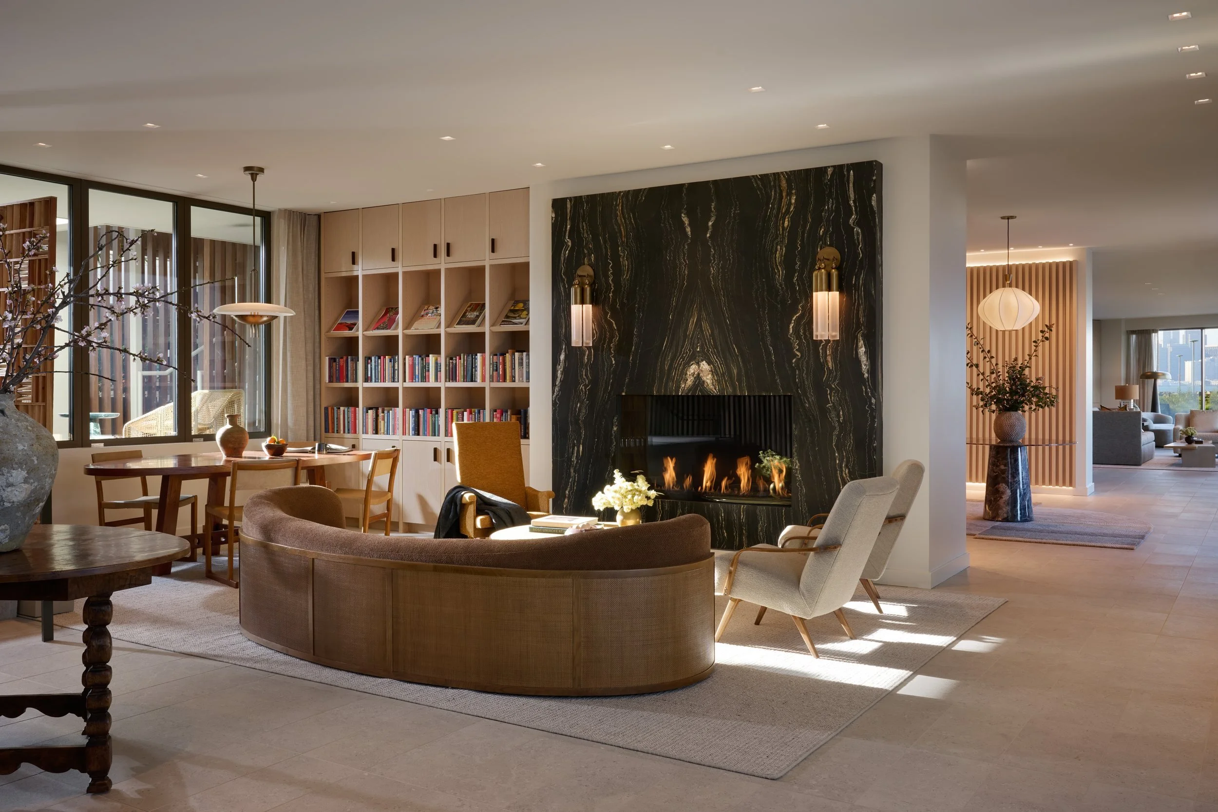Resident lounge with a curved sofa, book-lined shelves and a dark stone fireplace, 490 Avenue of the Palms, Treasure Island