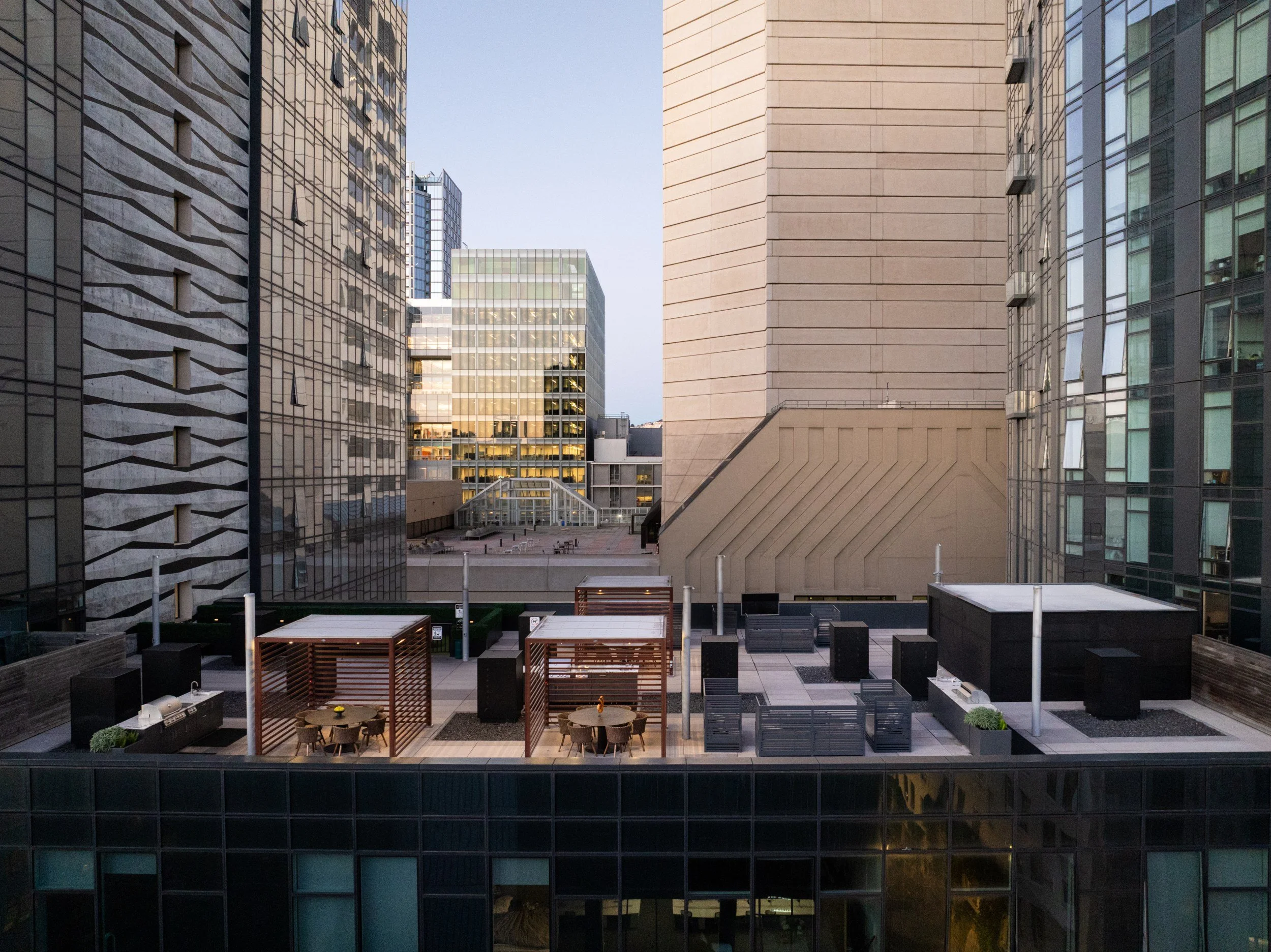 Rooftop deck with cabanas, grills and dining tables between towers at dusk, NEMA, San Francisco