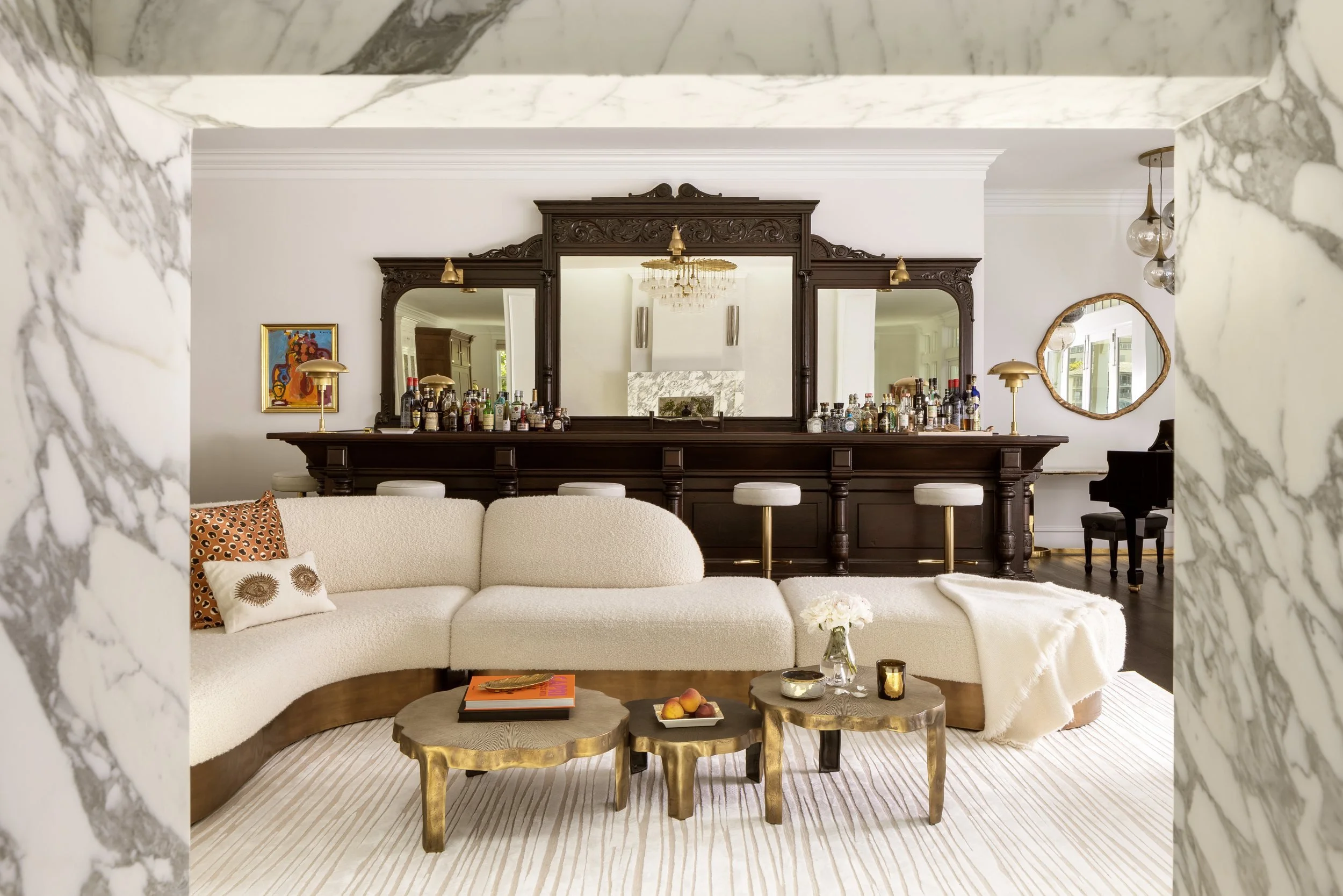 Lounge framed in Calacatta marble with a curved cream sofa before the carved wood back bar and mirrors, Valhalla, Sausalito