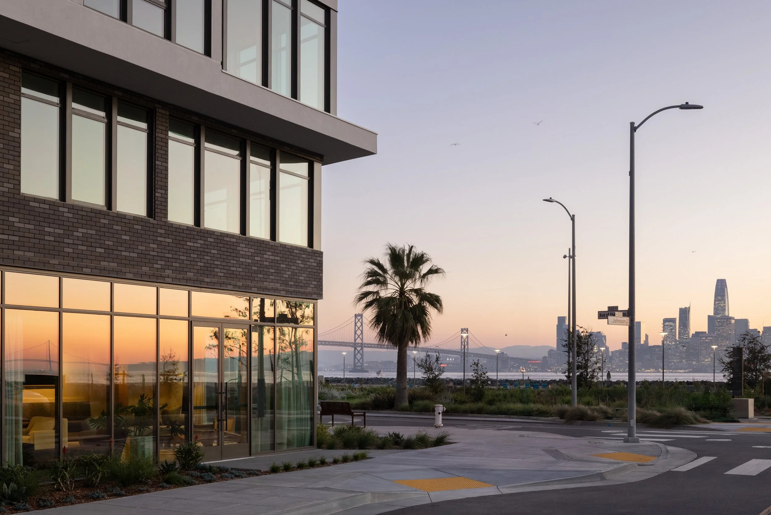 Building corner at sunset with a palm, the Bay Bridge and the San Francisco skyline across the water, 490 Avenue of the Palms, Treasure Island