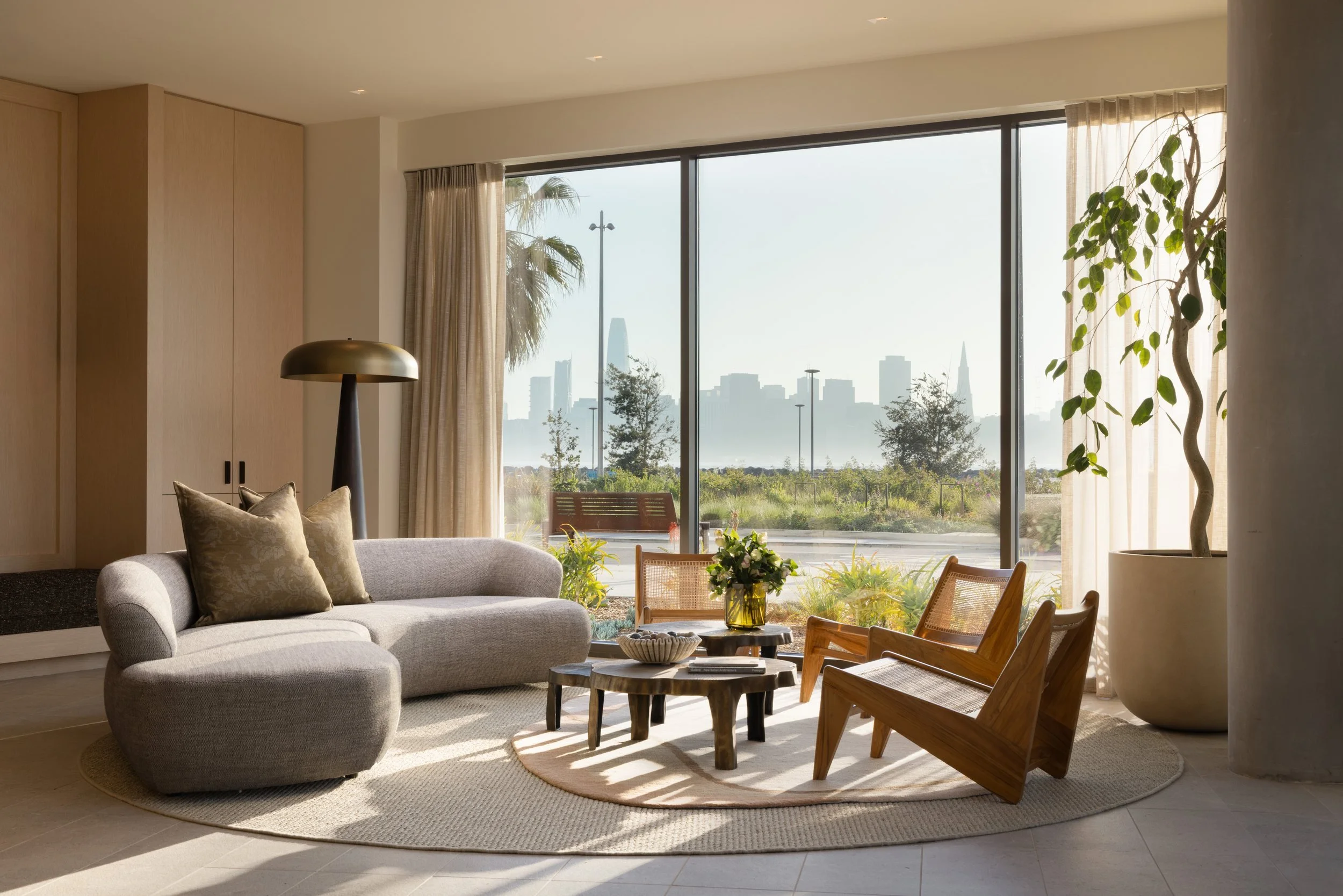 Residence living room with a curved boucle sofa and wood lounge chairs facing the San Francisco skyline, 490 Avenue of the Palms, Treasure Island