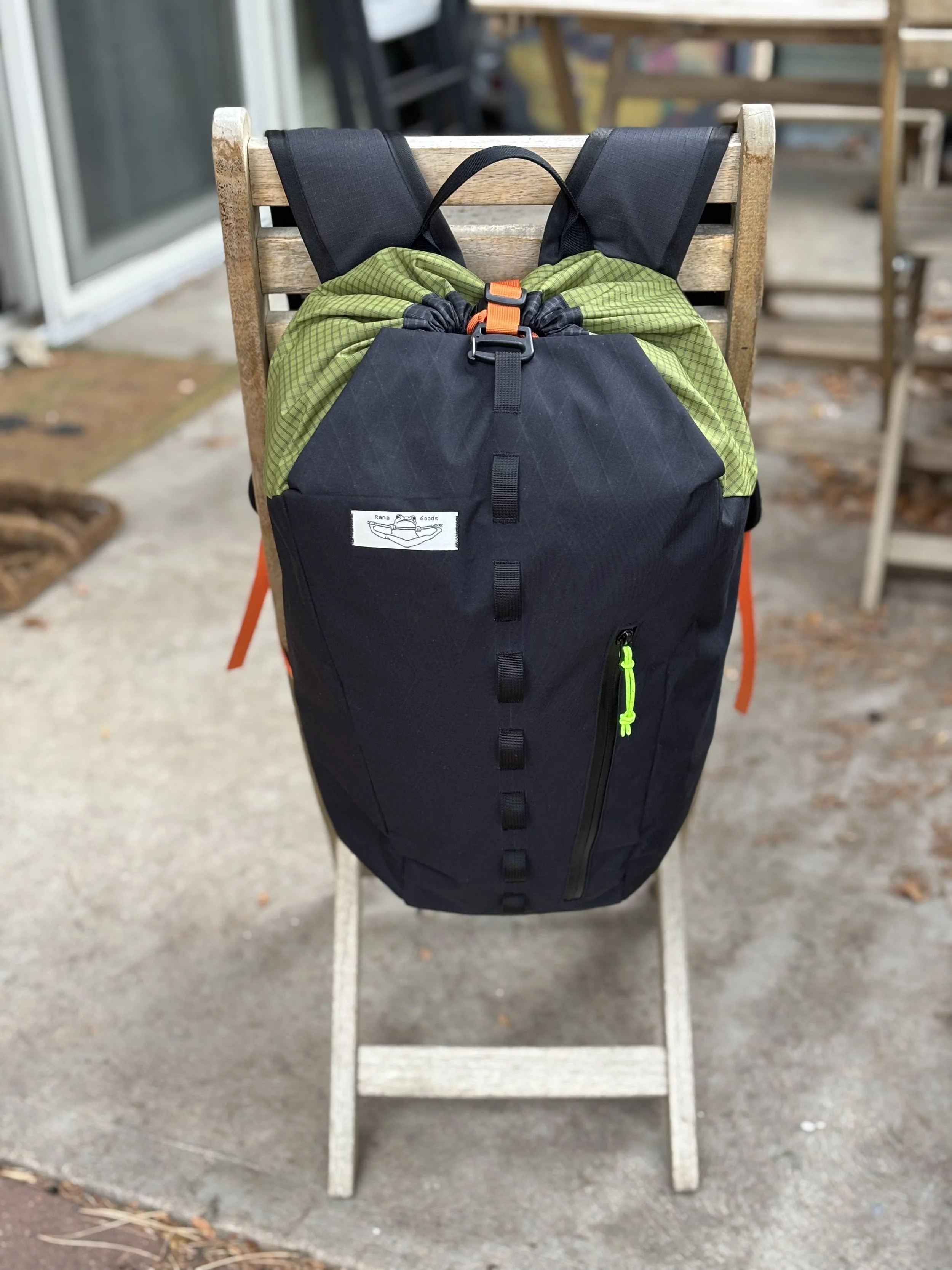 Black and green hiking backpack with orange straps resting on a wooden chair outdoors