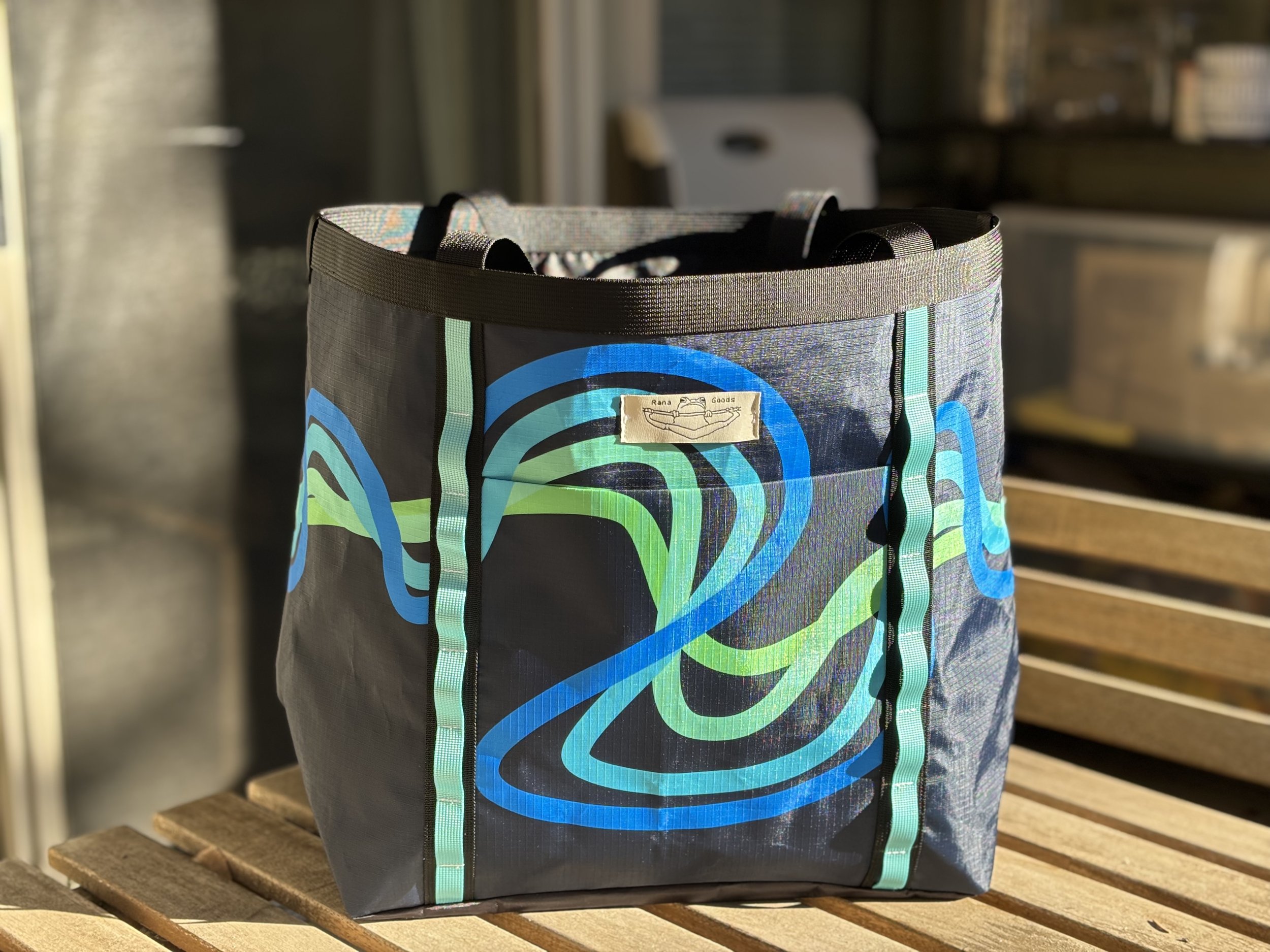 Colorful reusable tote bag with blue and green abstract wave design on a wooden bench.