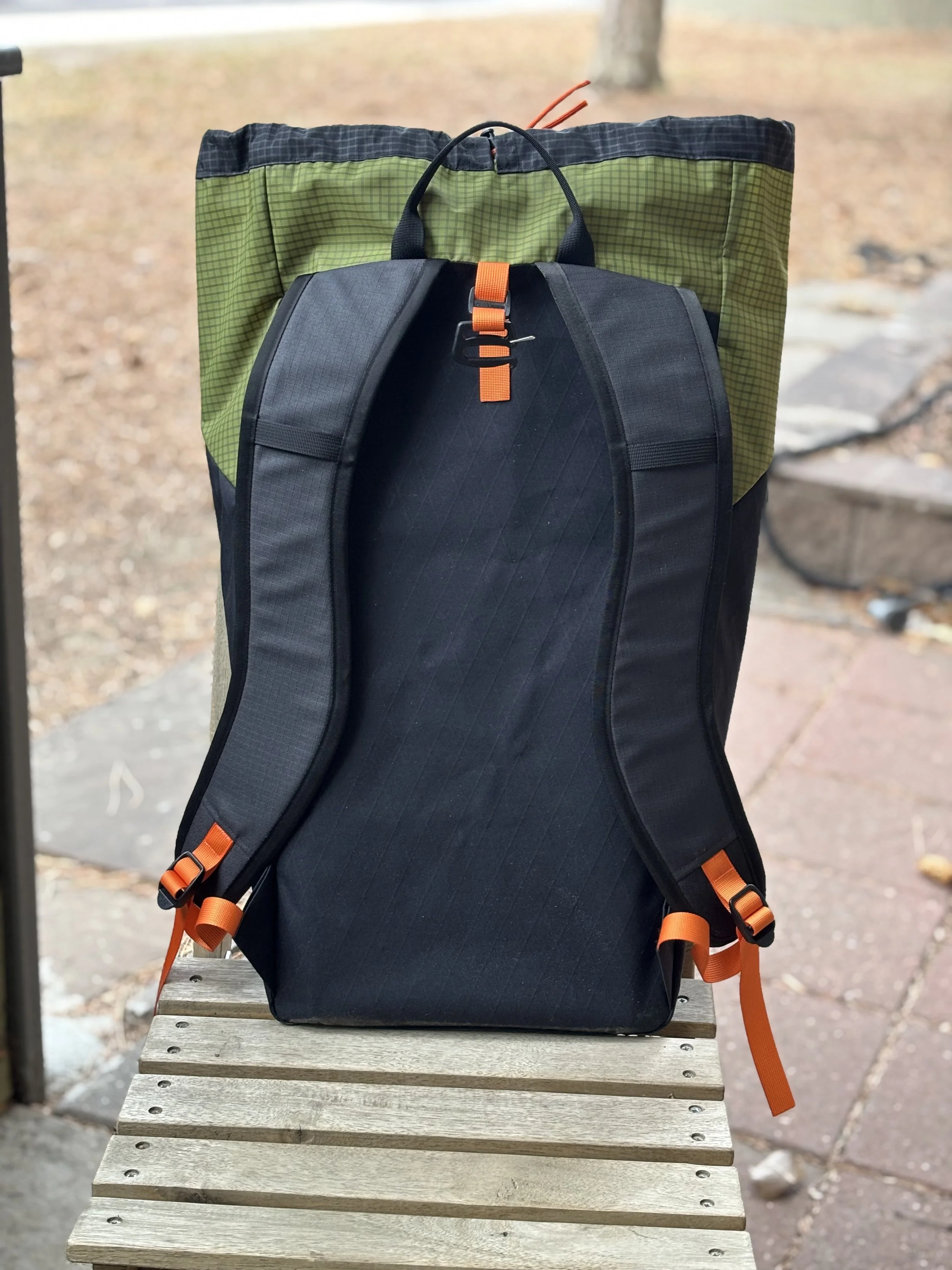 Black and green hiking backpack with orange straps resting on a wooden bench outdoors