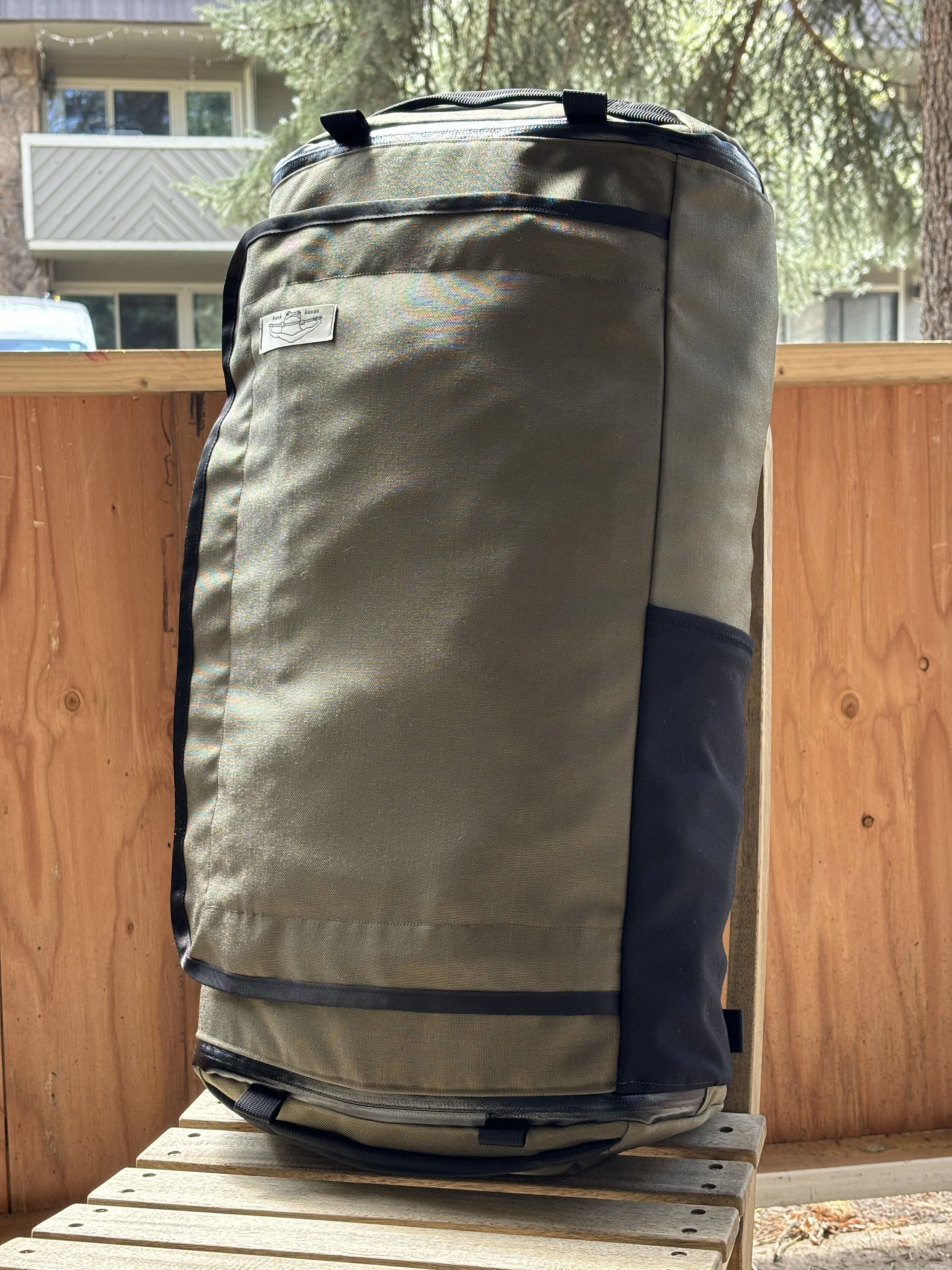 Olive green and black backpack with a front mesh pocket on a wooden bench outdoors