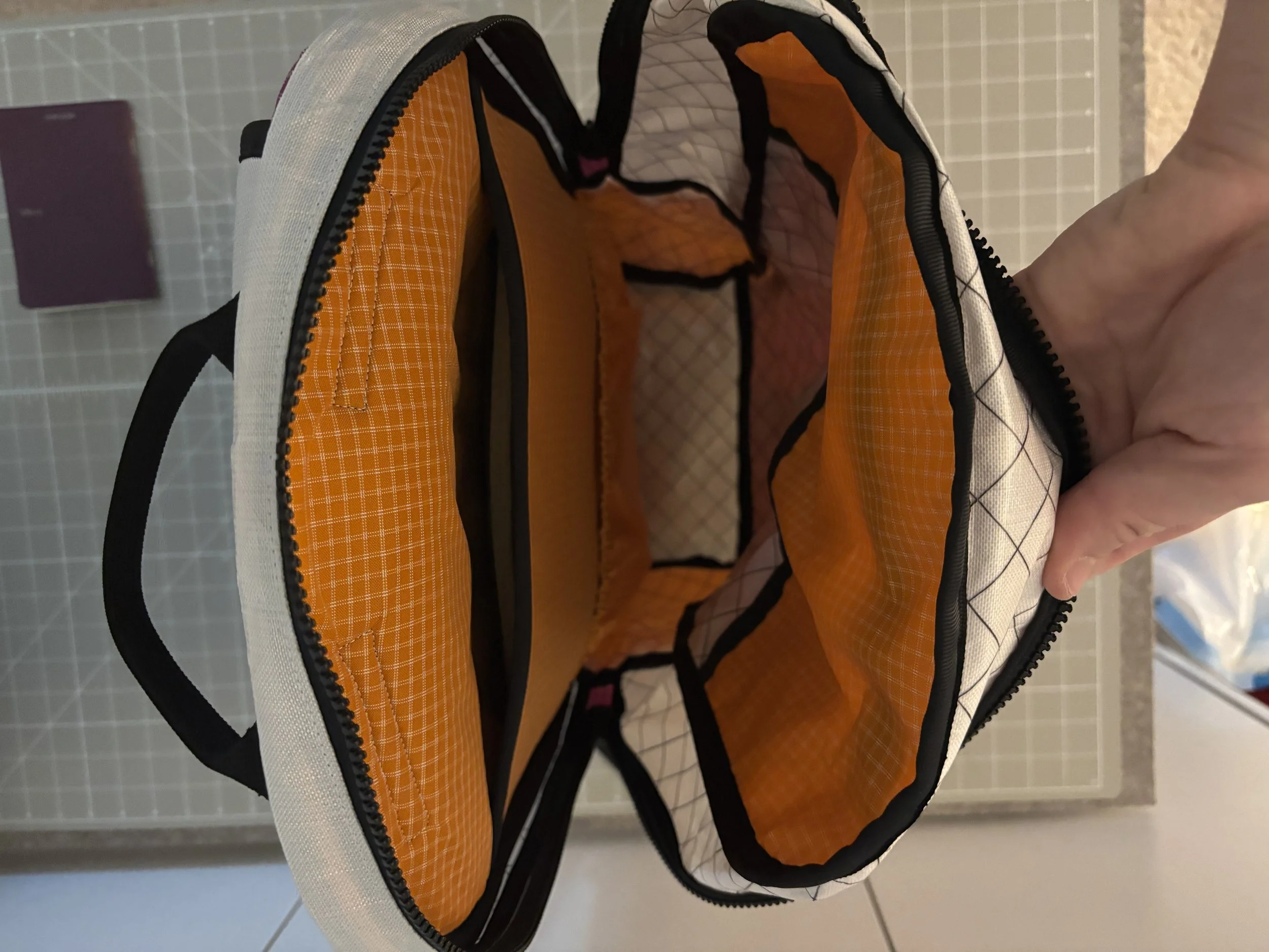 Open black, white, and orange backpack held by a hand, showing its spacious interior and zippered compartments.