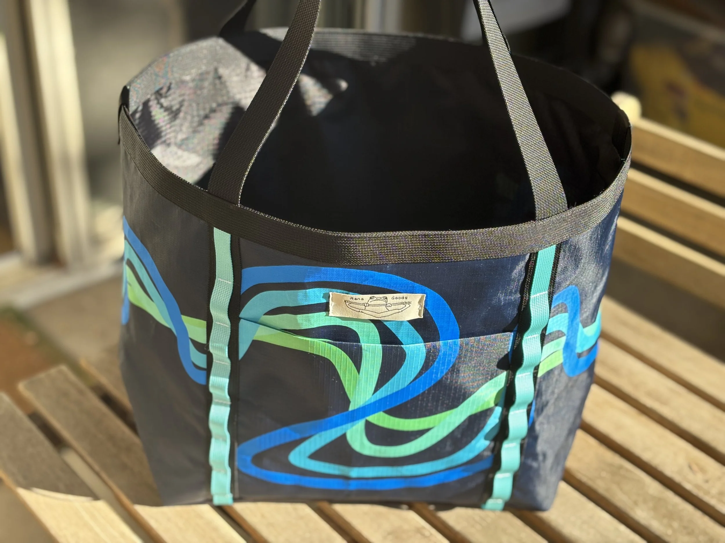 Colorful patterned fabric tote bag with black handles and turquoise straps on a wooden bench