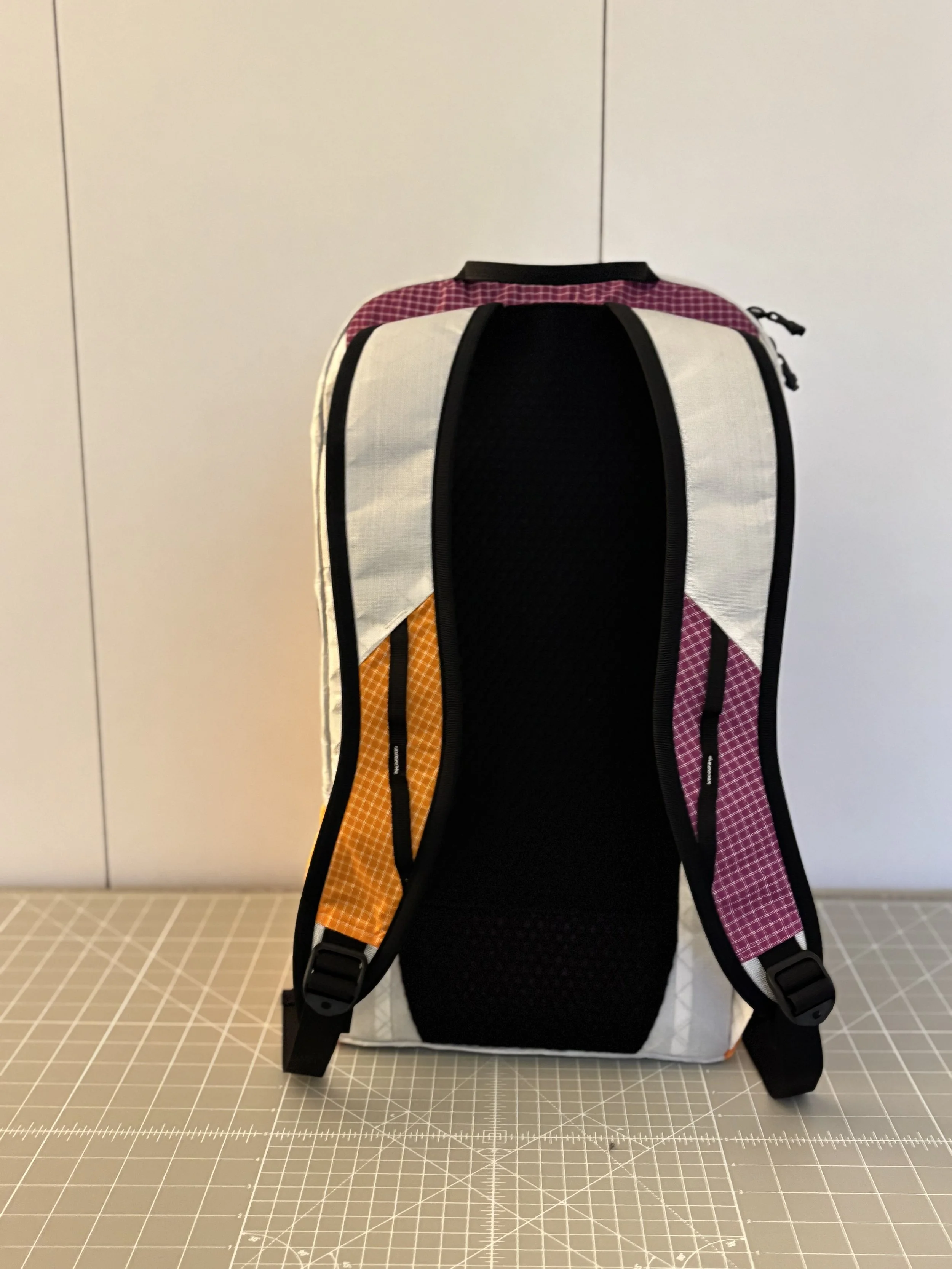 Black, white, orange, and purple handmade backpack displayed on a gridded cutting mat