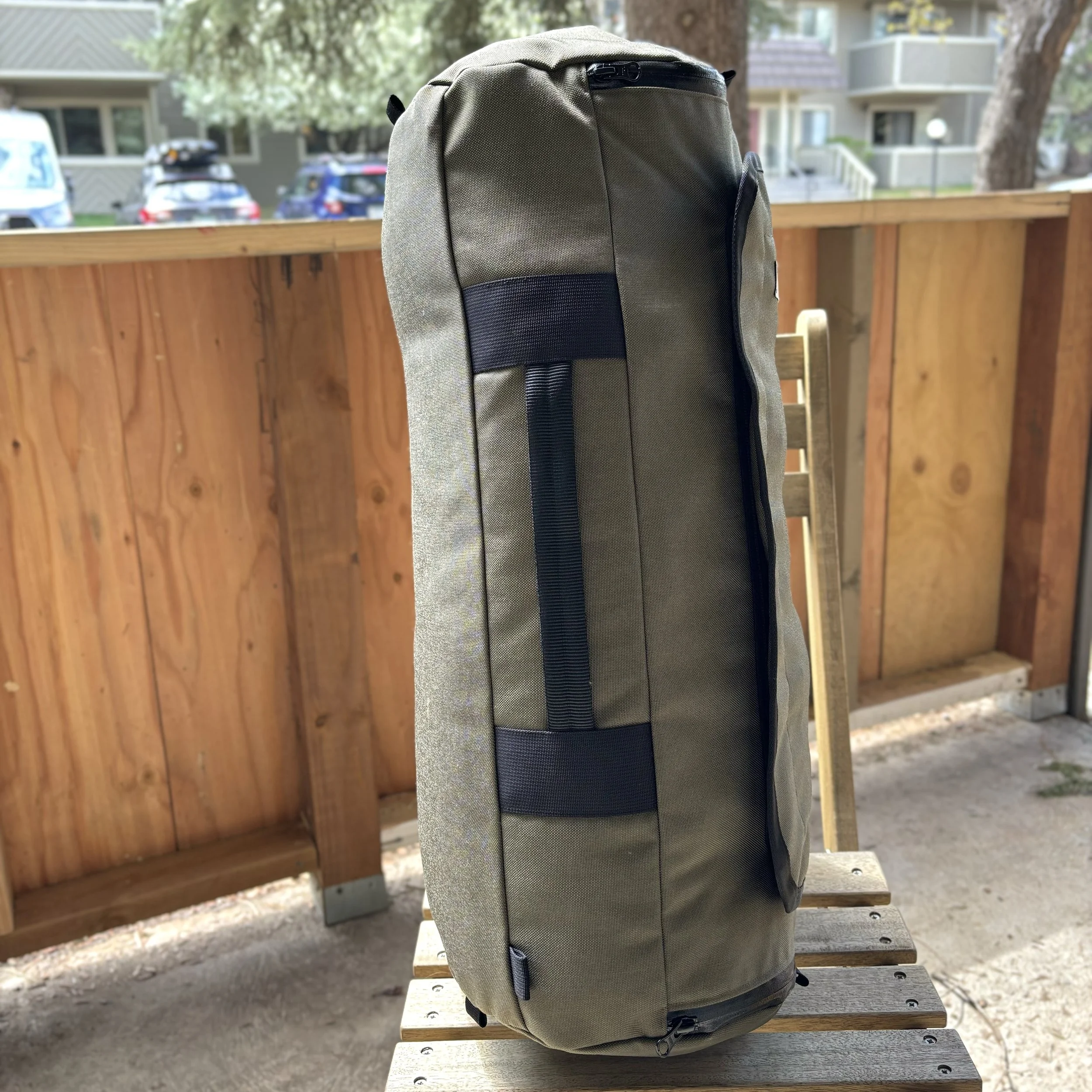 Olive green and black backpack resting on a wooden outdoor bench.