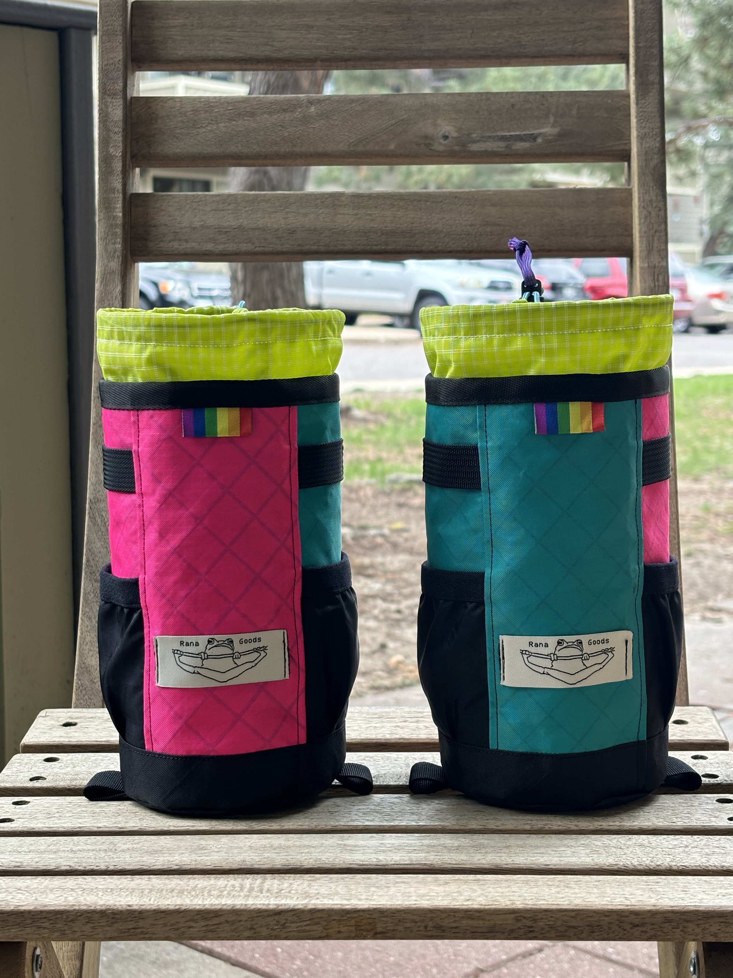 Two colorful handmade chalk bags with frog logo sitting on a wooden bench outdoors
