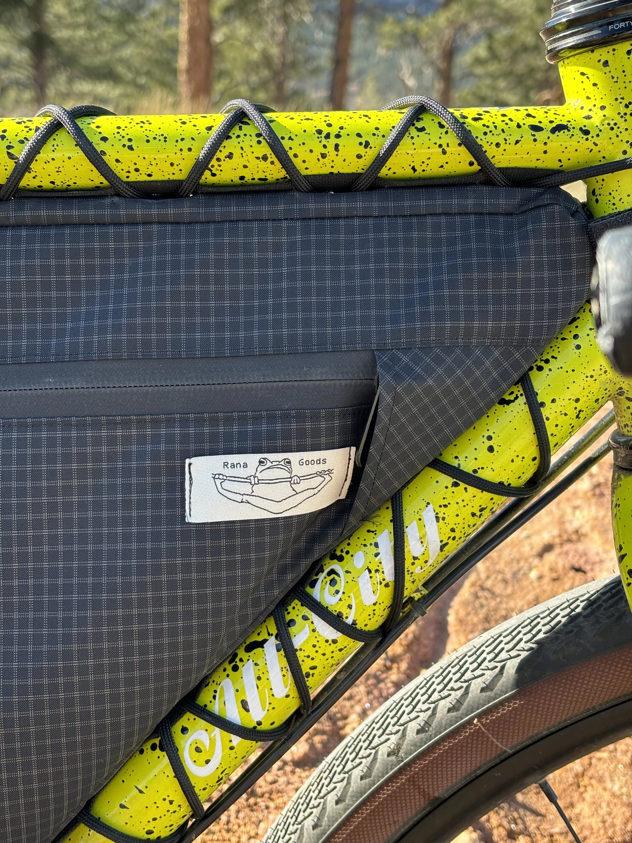 Black plaid bicycle pannier secured to a bright yellow, paint-splattered bike frame with bungee cords