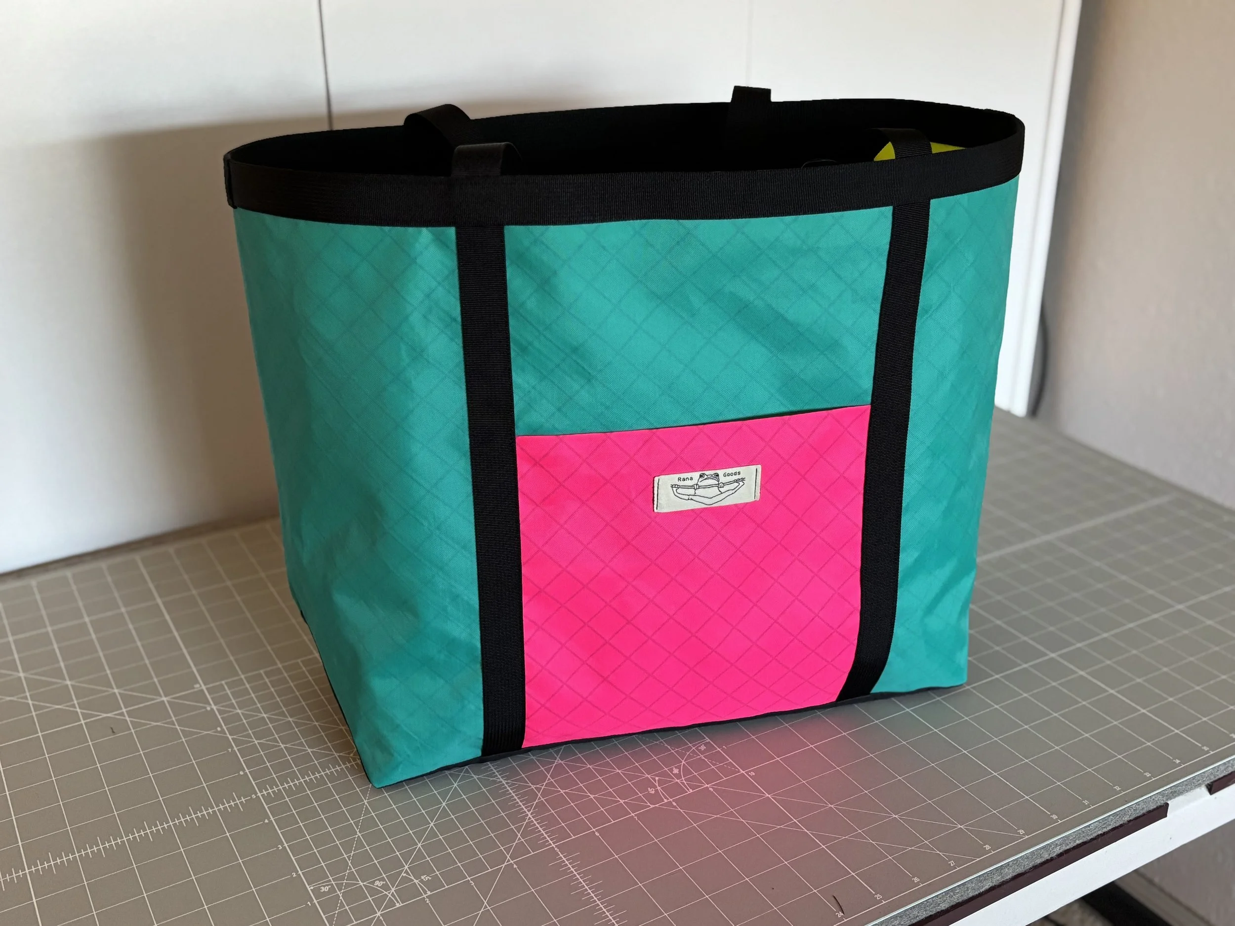 Turquoise and pink quilted tote bag with black straps on a cutting mat