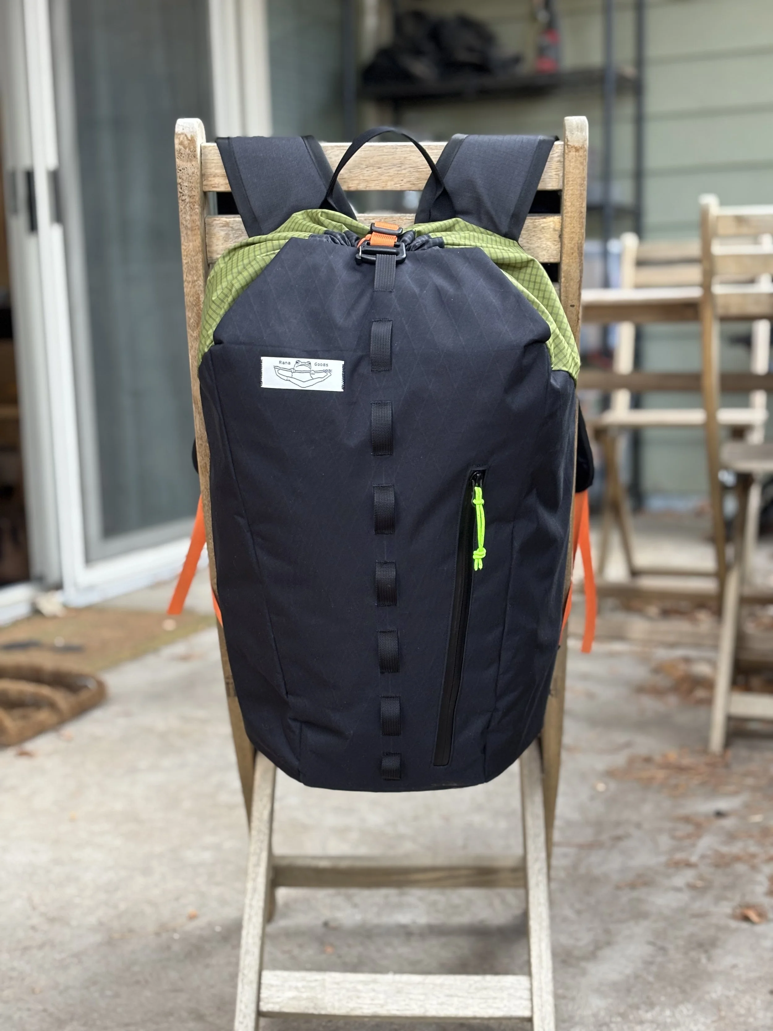 Navy blue hiking backpack with green lining and orange buckles hanging on a wooden chair