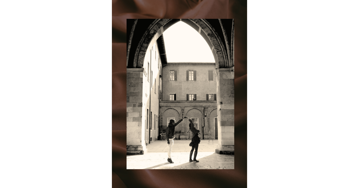 Sepia-toned photo of a couple dancing under a historic stone archway, evoking romantic nostalgia.