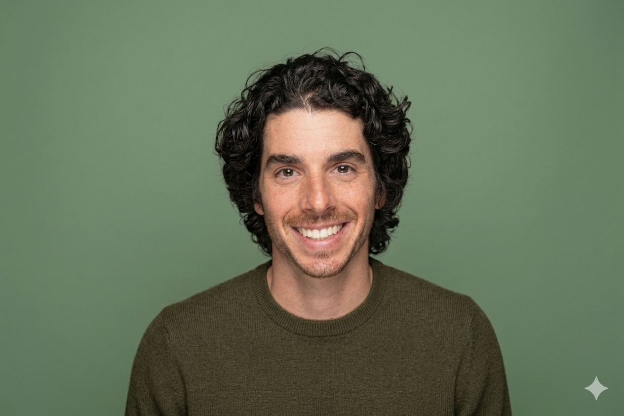 Smiling man with curly dark hair wearing a brown sweater against a green background