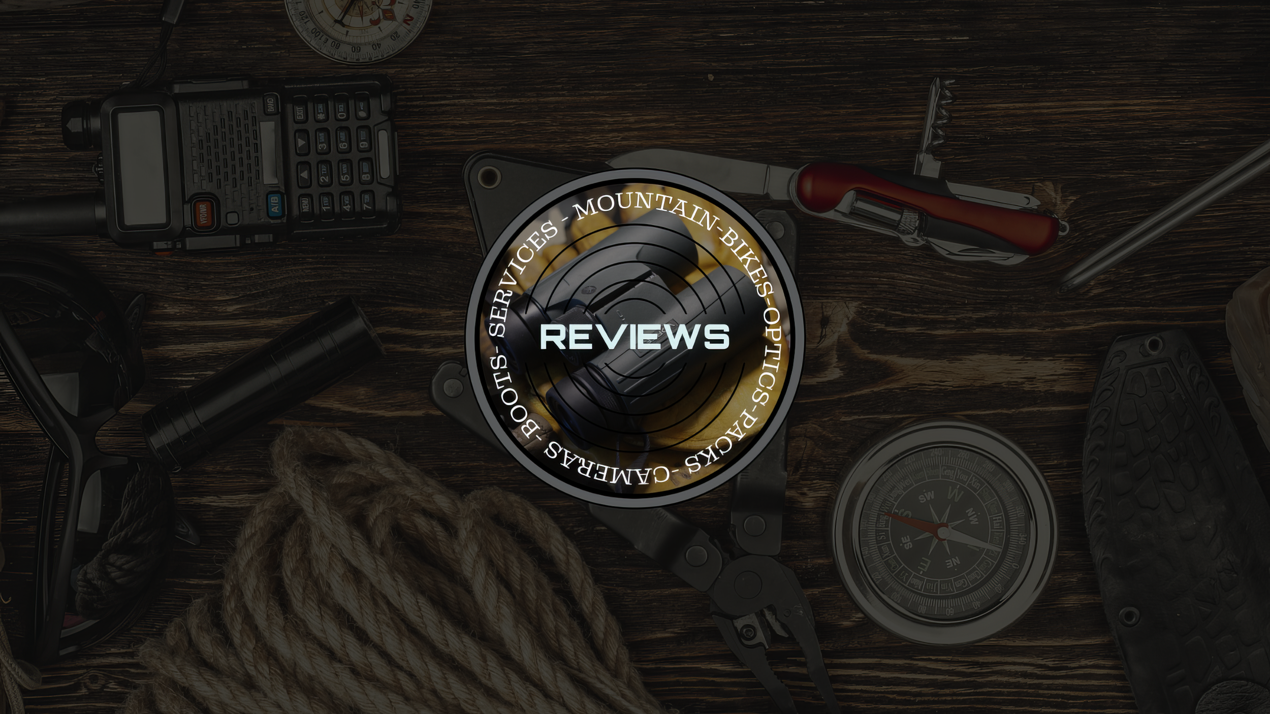 Outdoor gear arranged on a dark wooden table with a walkie-talkie, compass, climbing rope, carabiner, multitool, and boot surrounding a central “Reviews” graphic