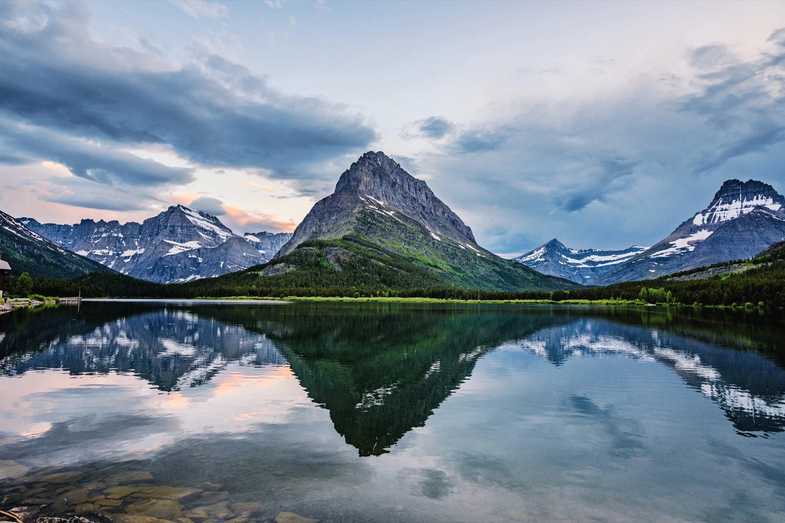 Snow-capped mountain range reflected in a calm alpine lake beneath a cloudy sky