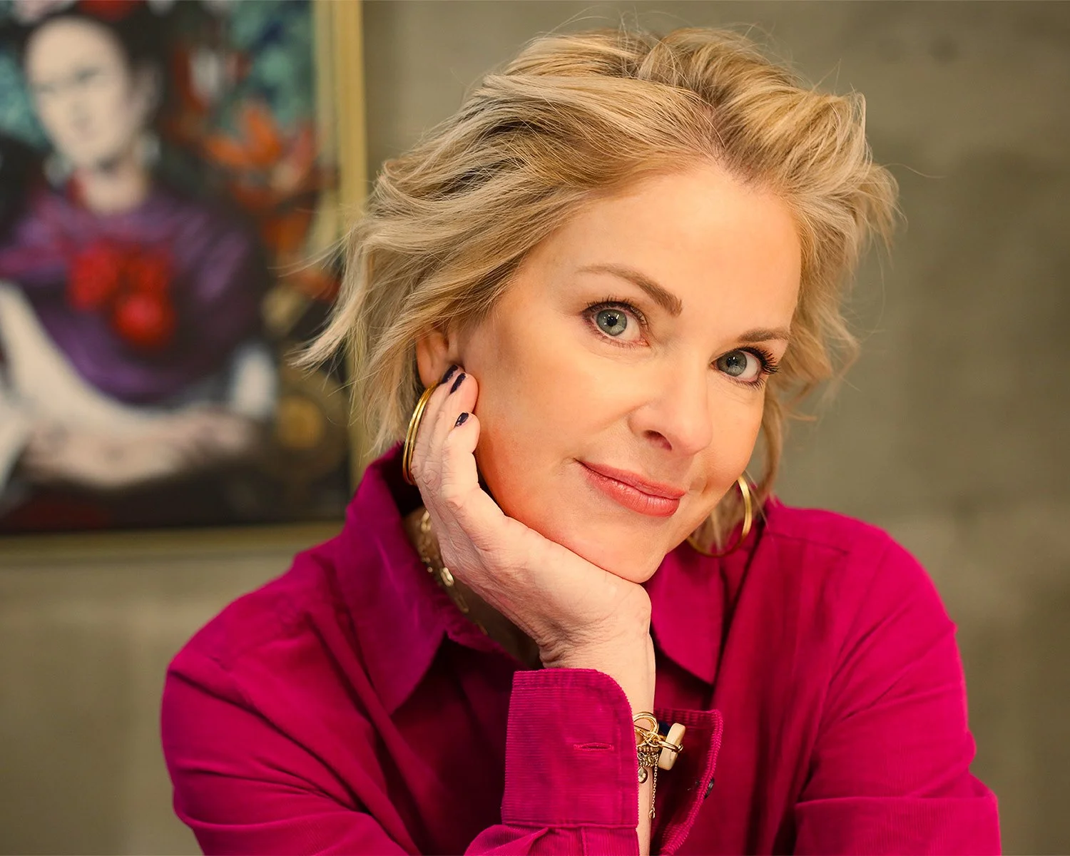 Smiling blonde woman in a magenta shirt resting her face on her hand