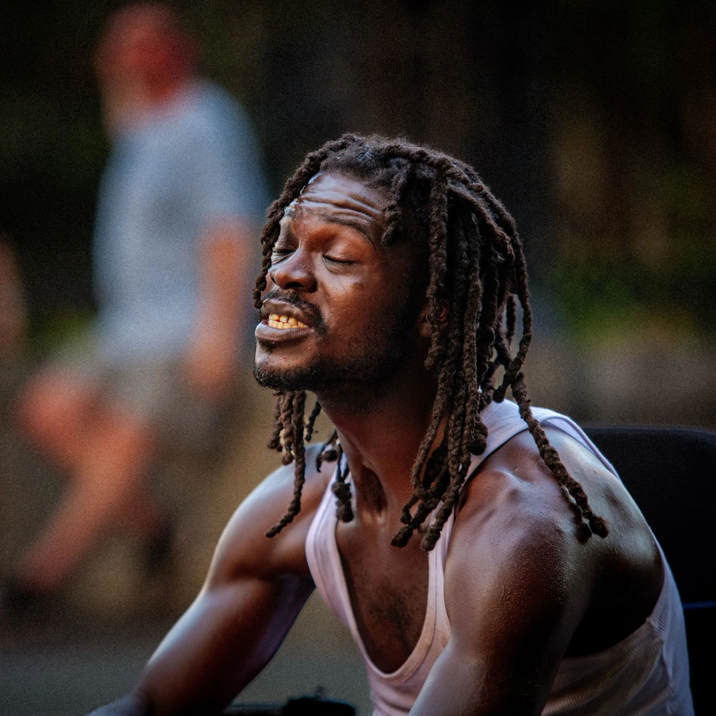 Close-up of a Black man with long dreadlocks and closed eyes wearing a white tank top.
