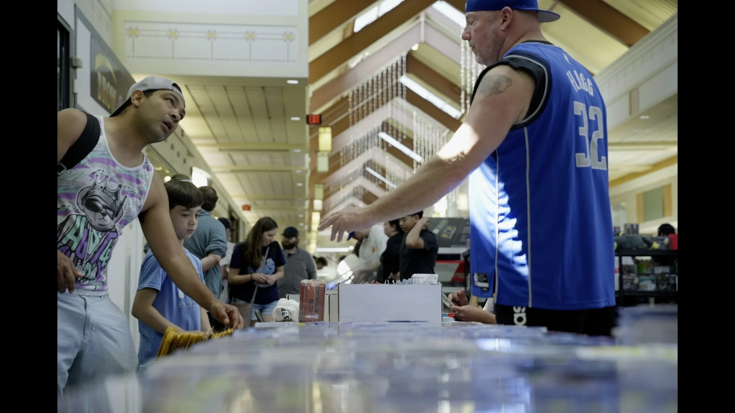 Man in a blue basketball jersey interacting with shoppers at a mall counter