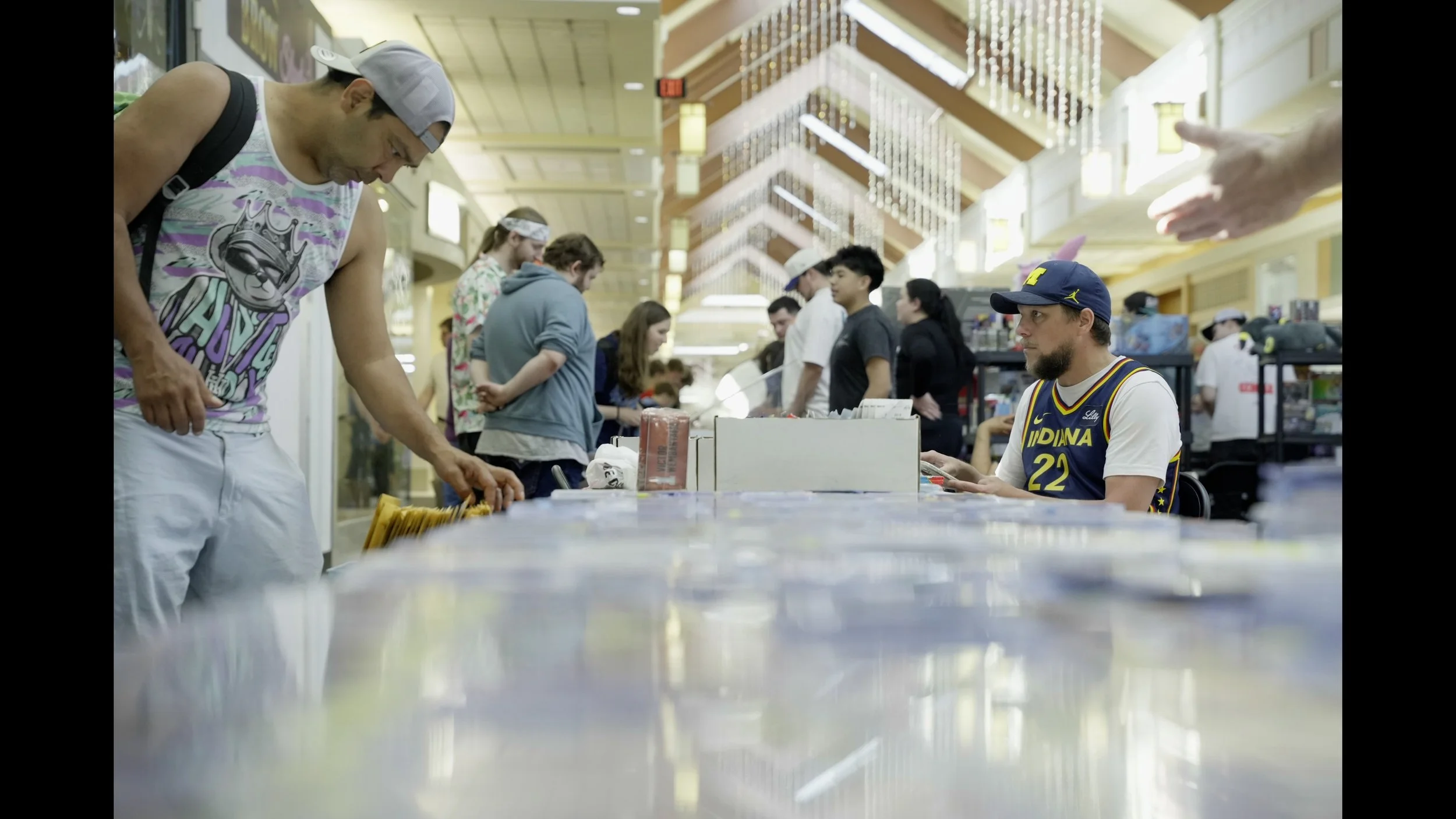 People browse merchandise at a busy indoor market, including a man wearing an Indiana basketball jersey and cap.