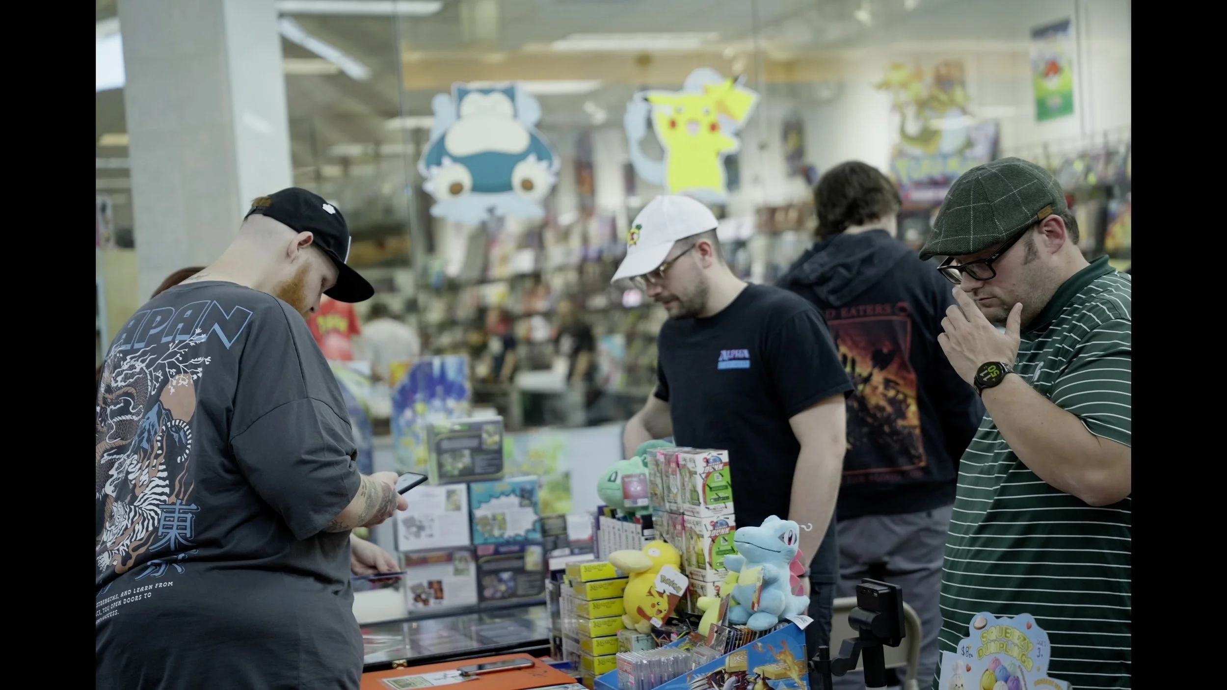 Four men browse Pokémon merchandise at a store counter.