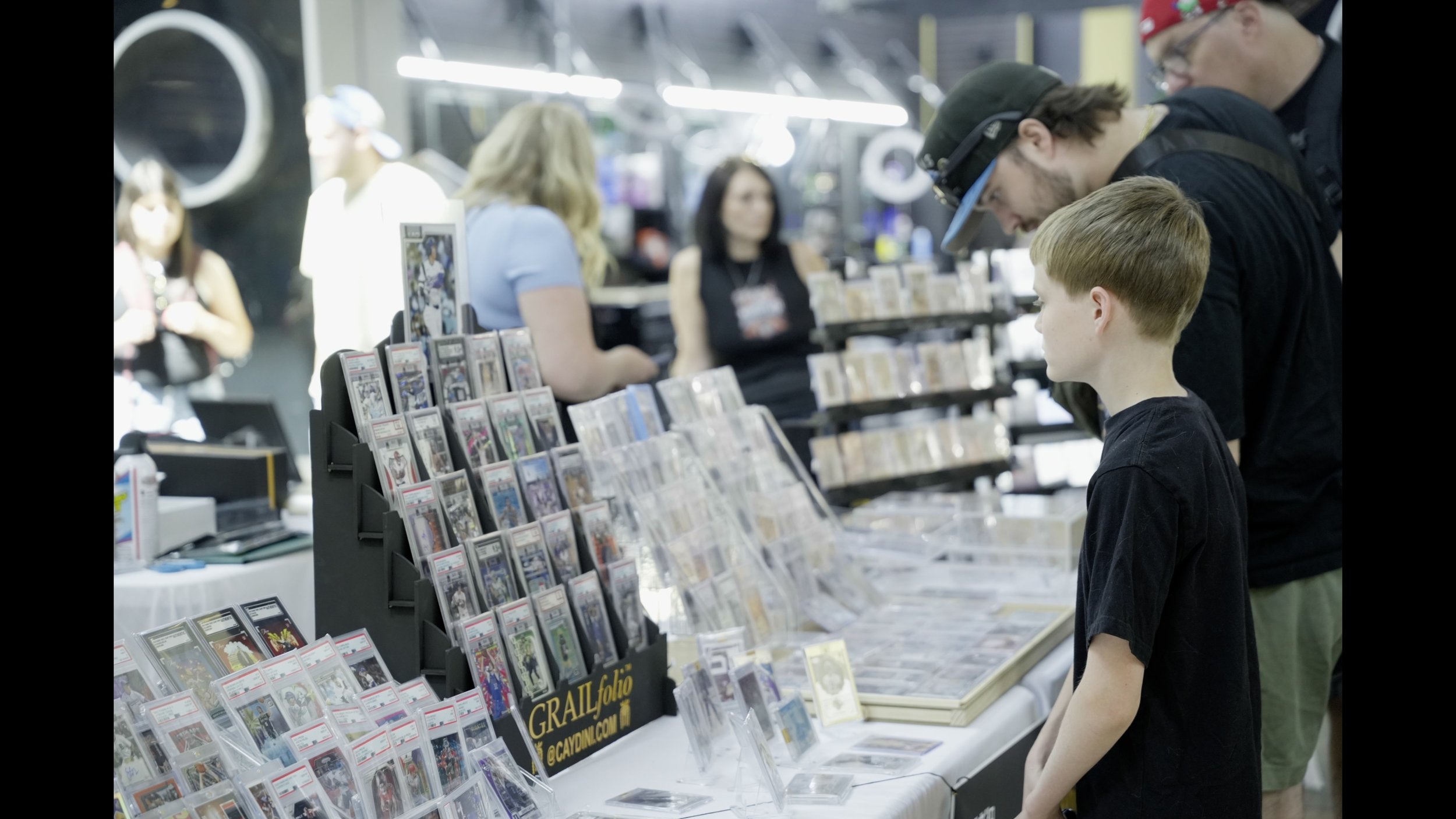 Young boy and adults browsing graded comic books and collectibles at a convention vendor booth