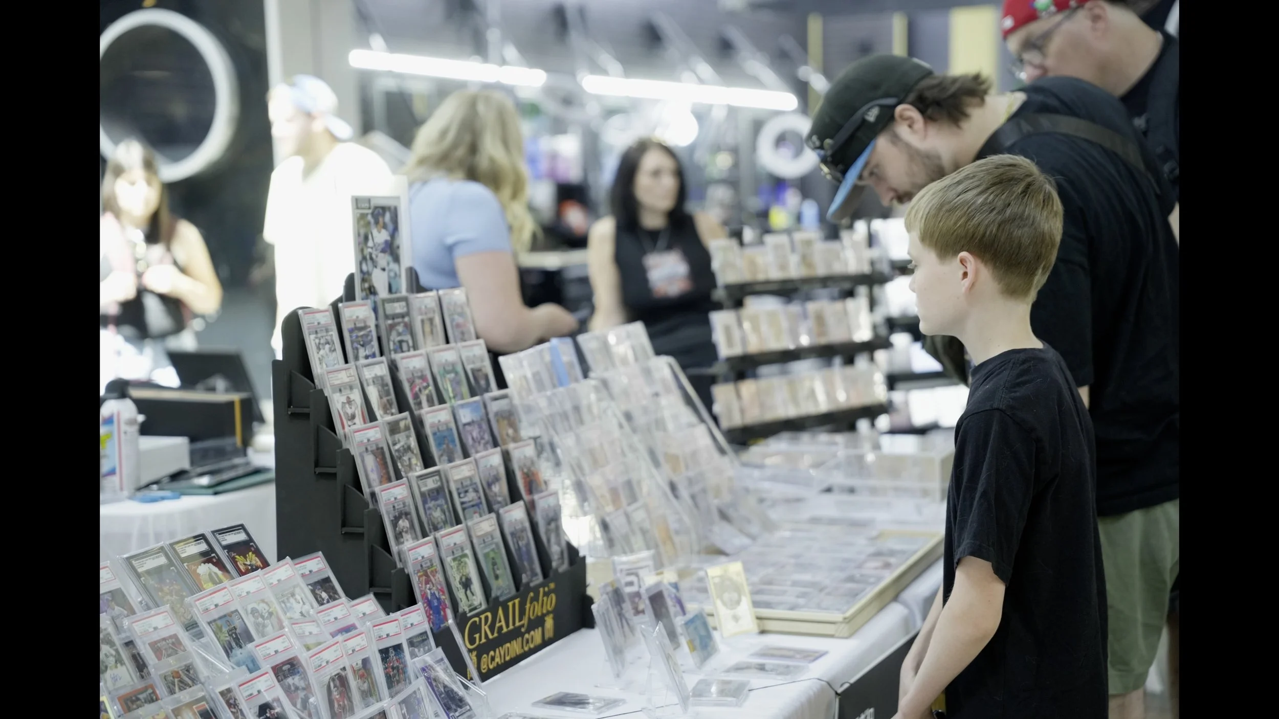 A boy browses graded comic books and collectibles at a busy convention vendor booth.