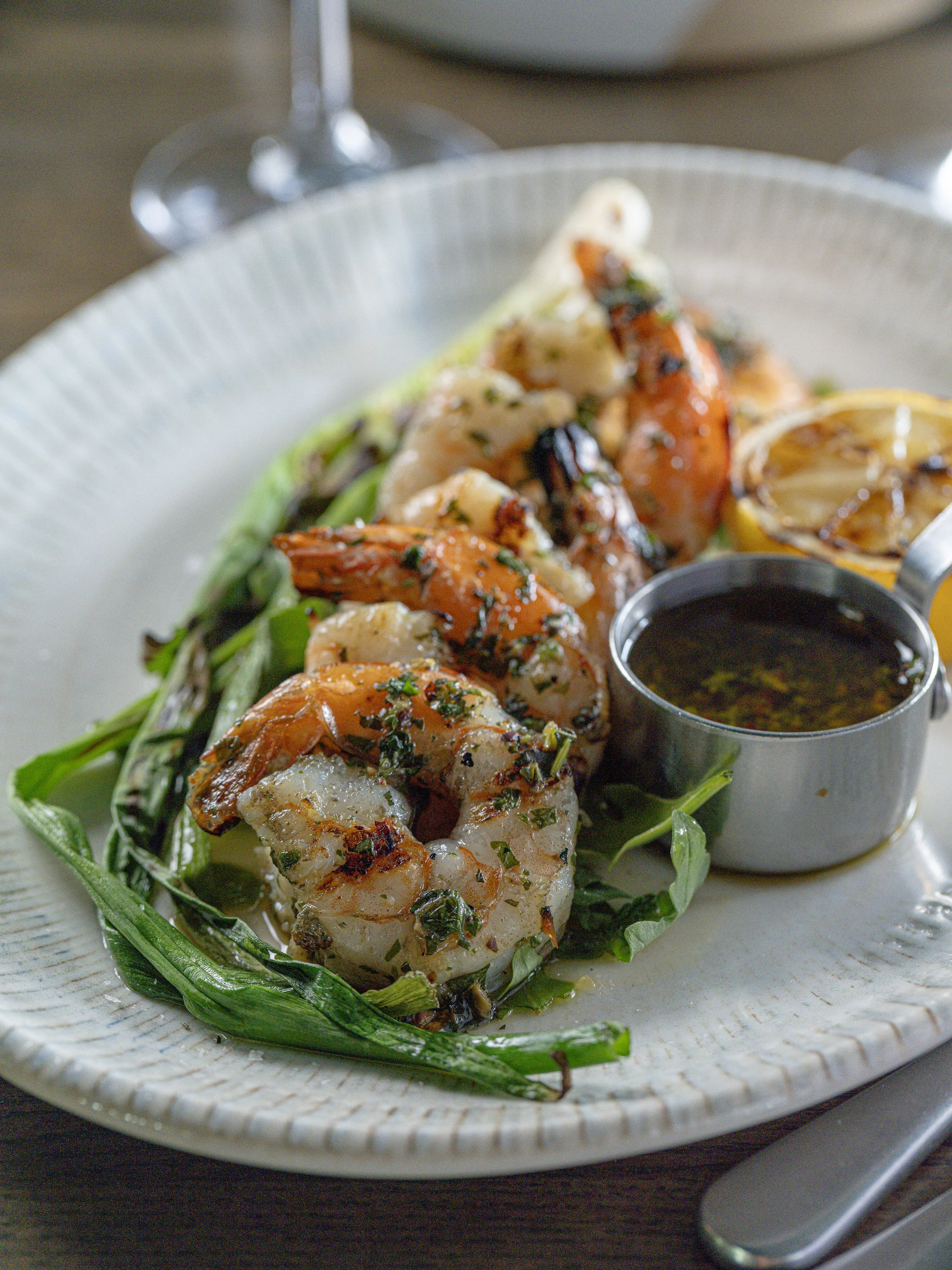 Close-up of grilled shrimp with herbs, vegetables, and dipping sauce on a plate