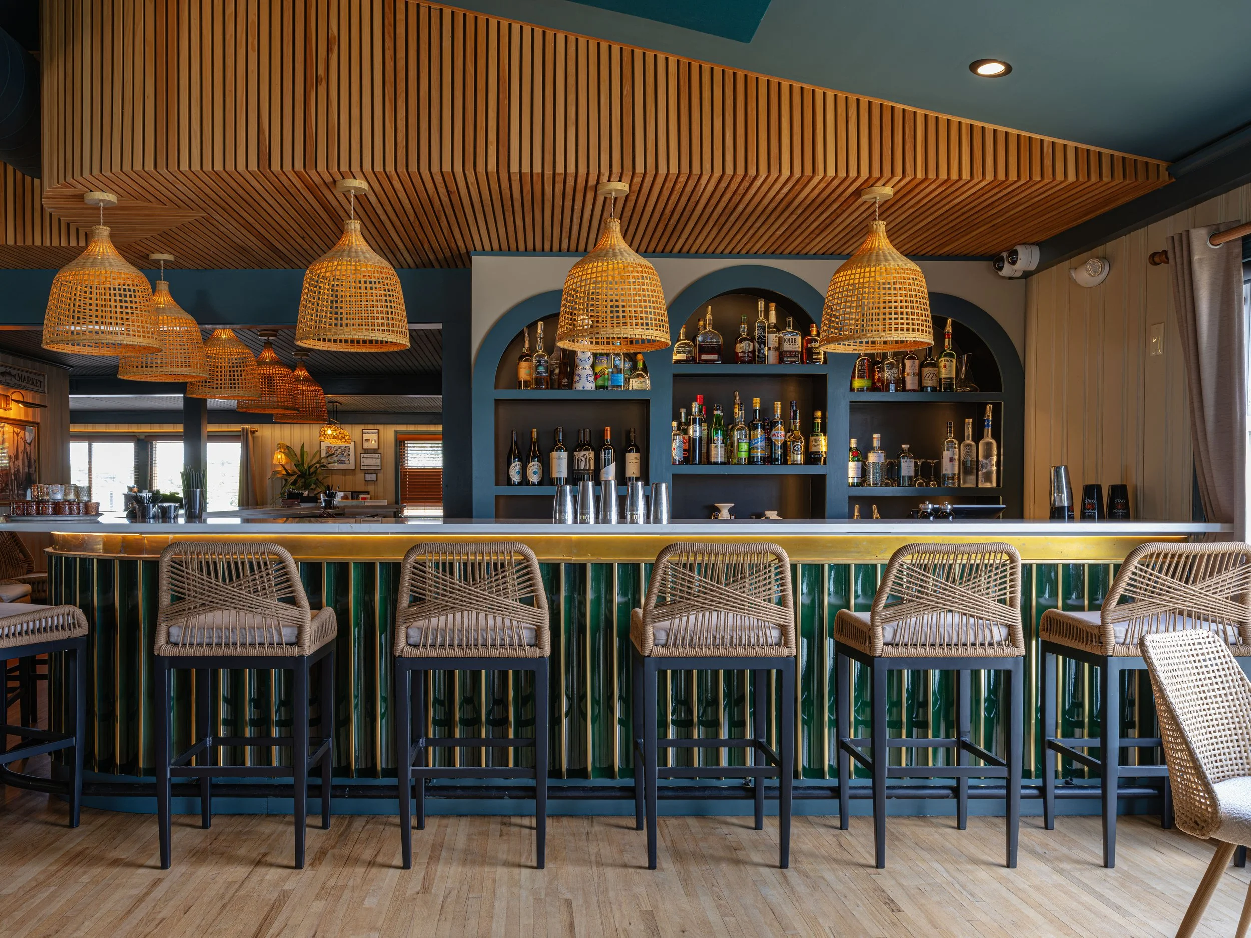 Stylish bar interior with liquor shelves, woven pendant lights, wood-slat ceiling, and rattan bar stools
