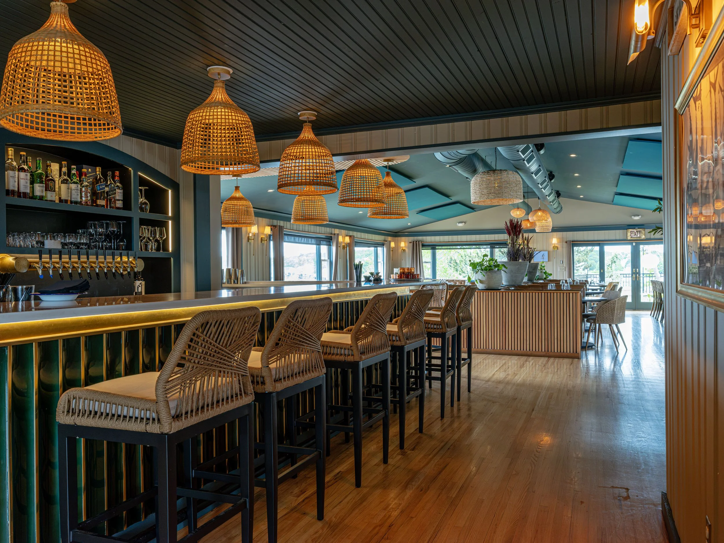 Stylish restaurant bar with wicker pendant lights, liquor shelves, high-top seating, and large windows