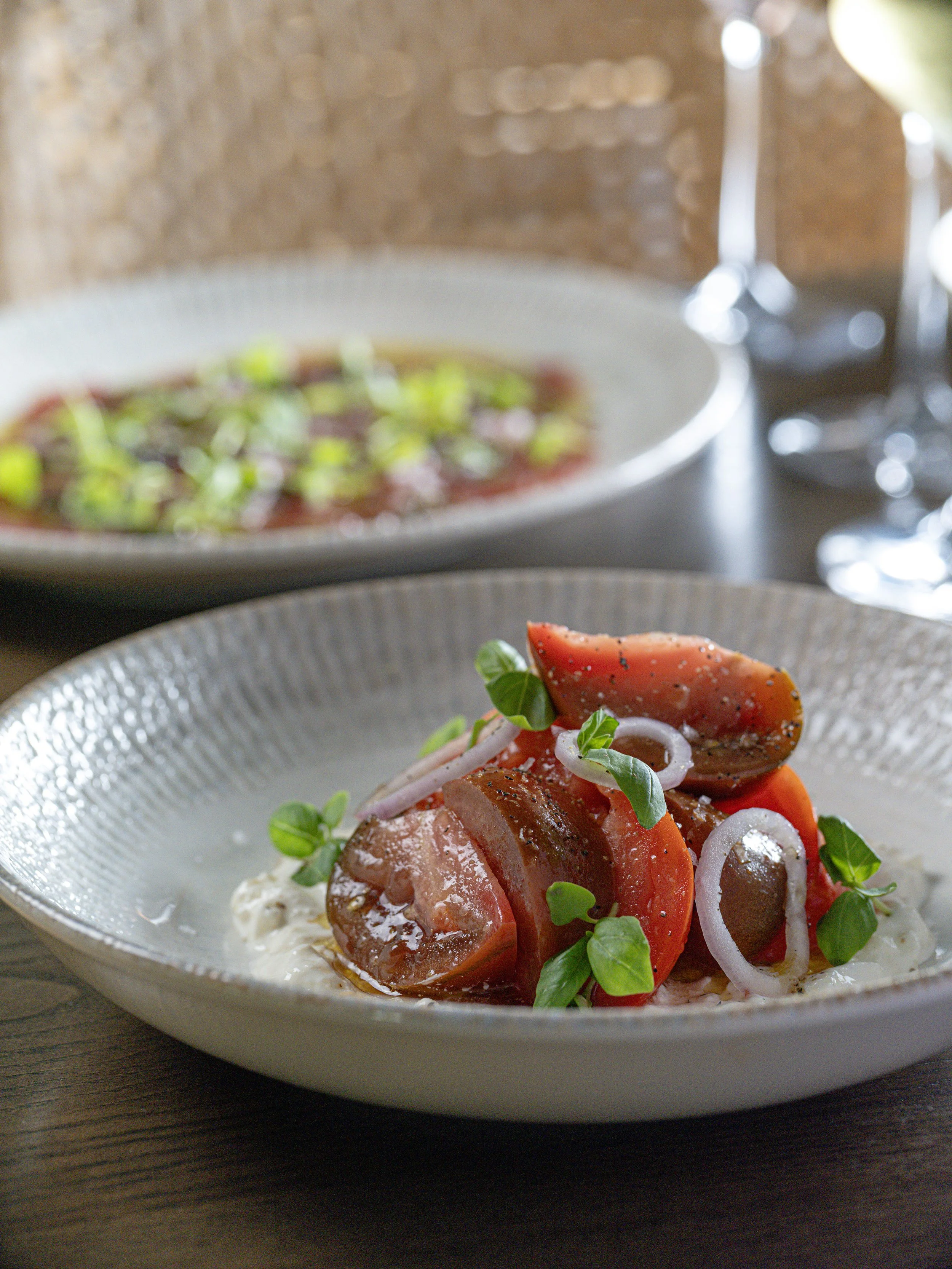 Close-up of a fresh tomato salad with red onions, greens, and herbs on a glass plate.