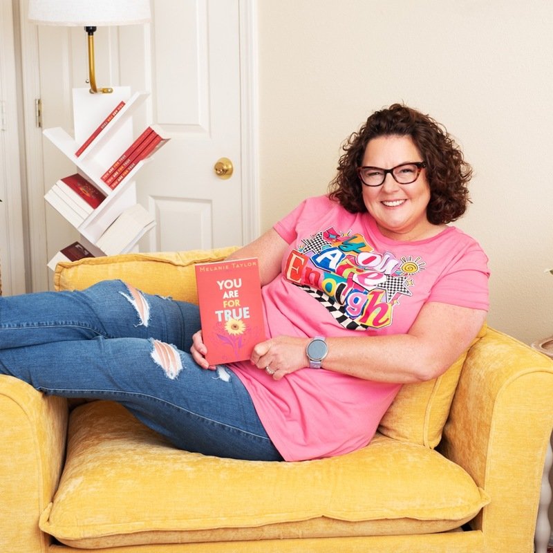 Melanie Taylor, LPC-S, smiling while seated in a yellow chair holding copy of You Are For True.