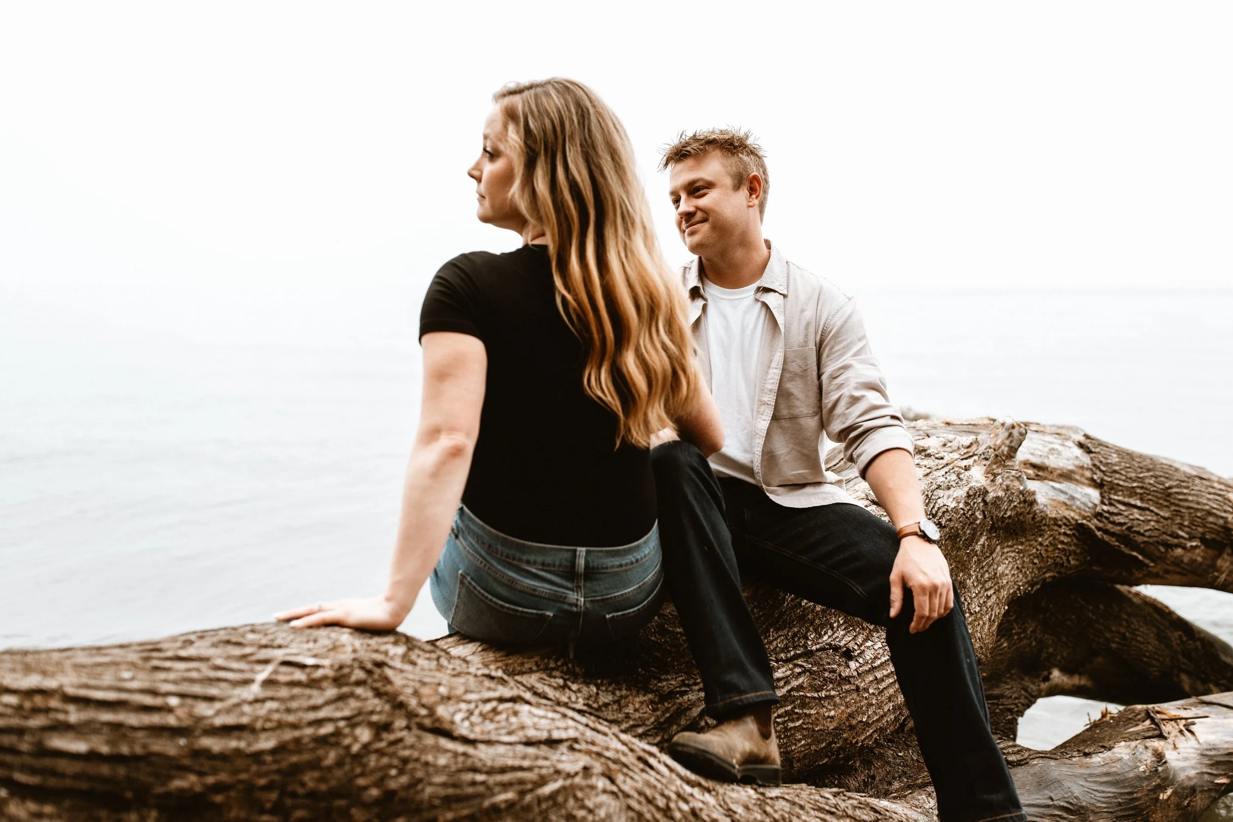 young couple sitting on downed tree by lake ontario 